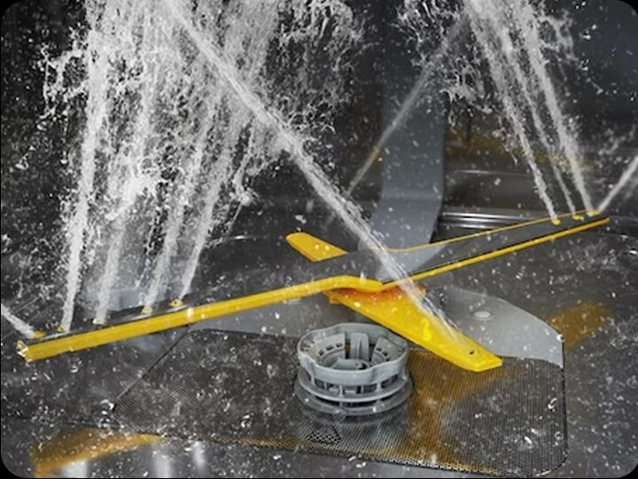 Wnętrze zmywarki z wodą rozpryskującą się z wielu kierunków na żółte części.