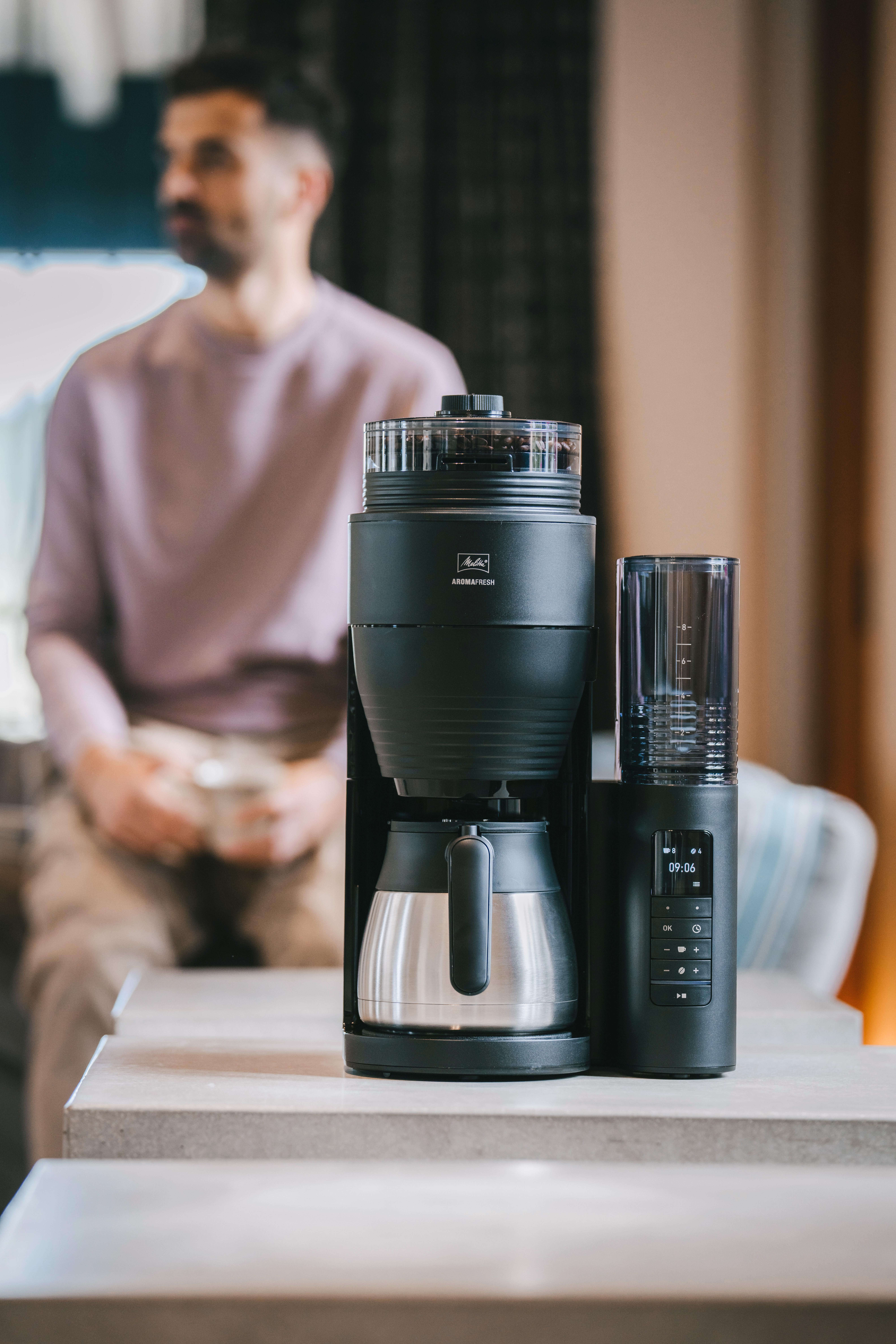 Eine schwarze Kaffeemaschine mit Stahlkanne. Mann im Hintergrund unscharf.