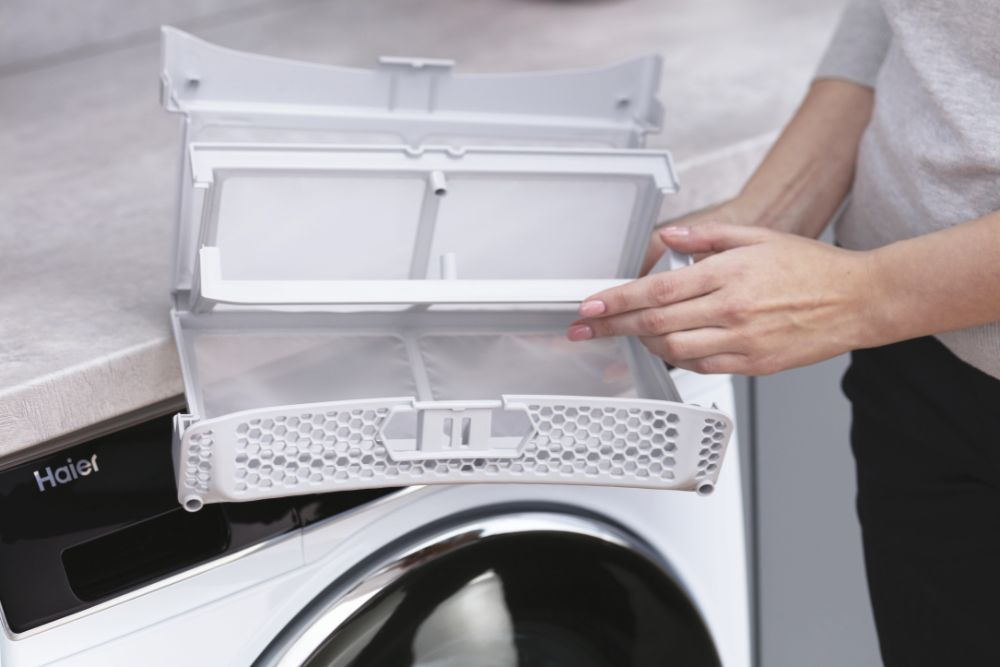 Les mains d'une personne ouvrent un filtre de sécheuse blanc pour nettoyer sur un comptoir.
