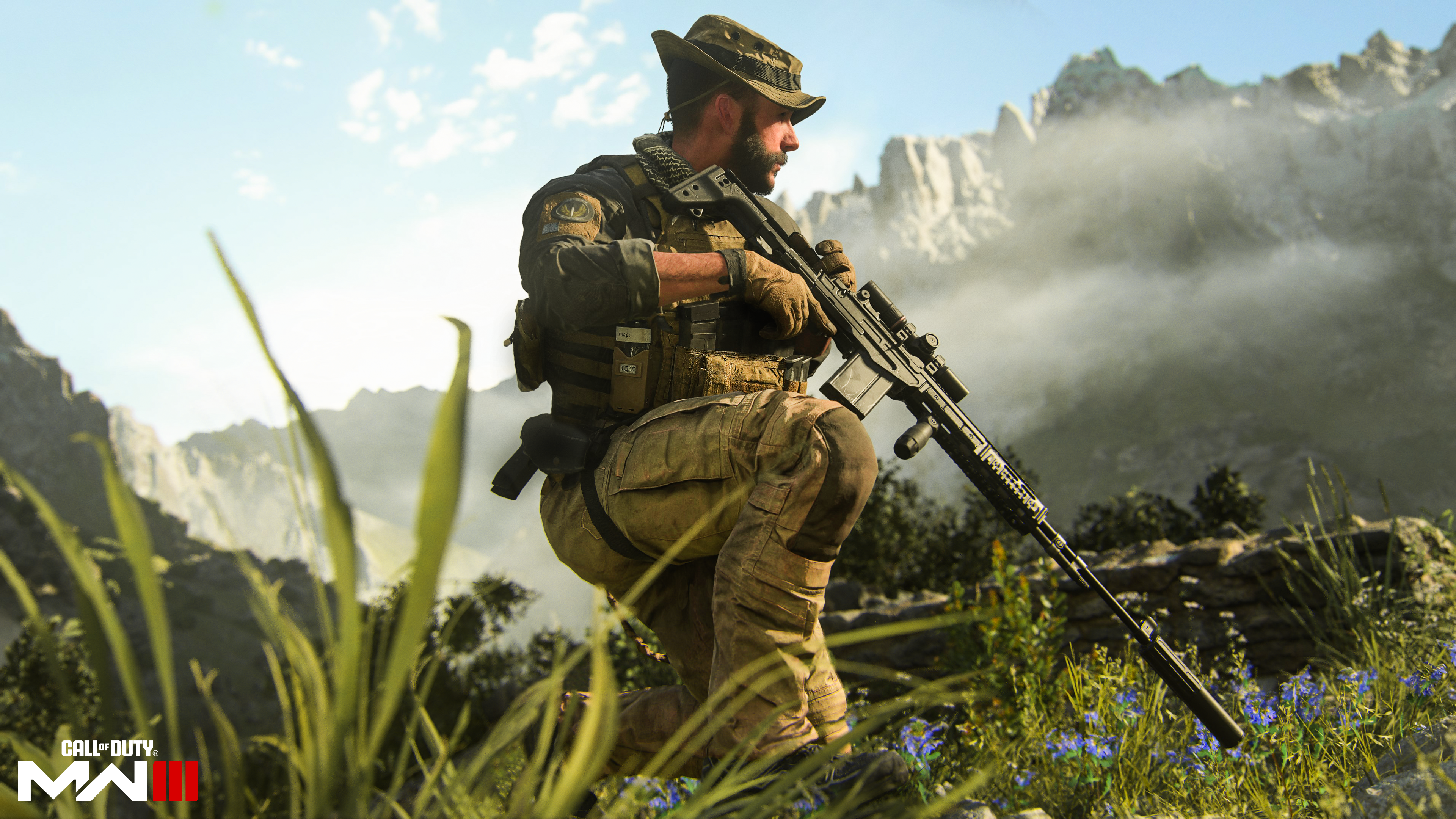 Un soldat s'agenouille avec un fusil dans un champ herbeux avec des montagnes en arrière-plan.