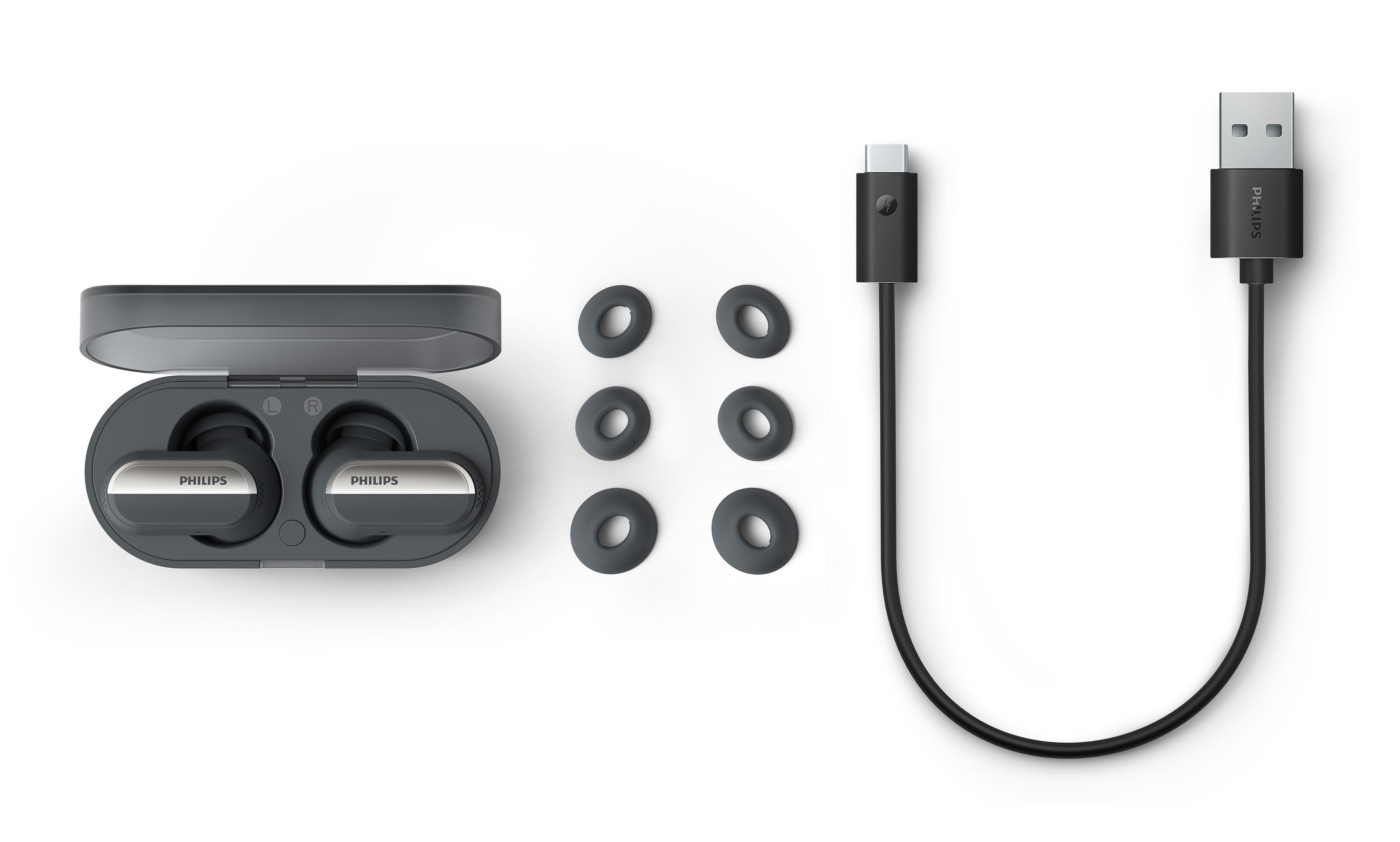 Ohrhörer, Ladecase und USB-Kabel. Ohrhörer sind grau, Ladecase ist dunkelgrau.