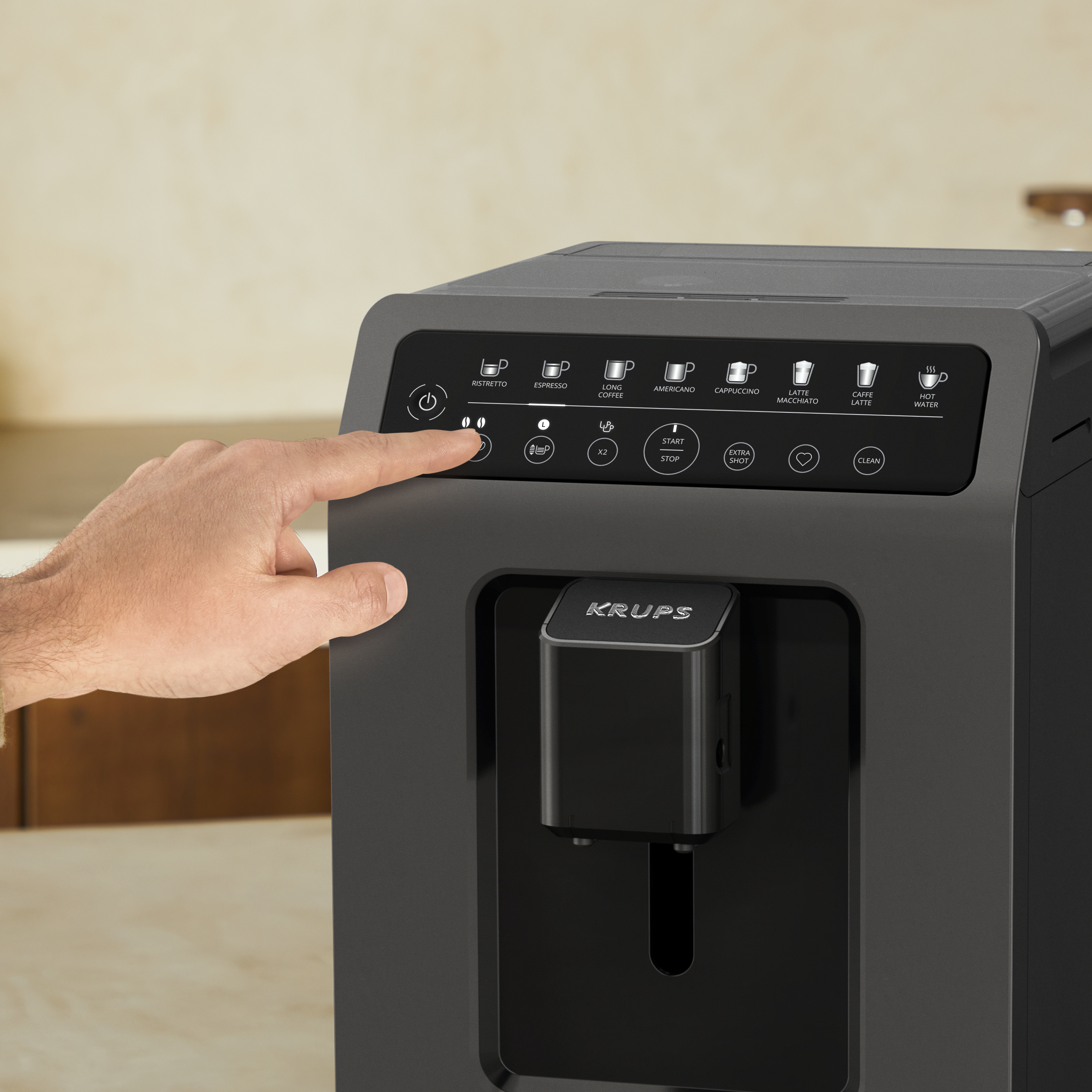 Die Hand einer Person drückt eine Taste auf einer Krups Kaffeemaschine. Die Maschine ist schwarz. Küchenhintergrund.