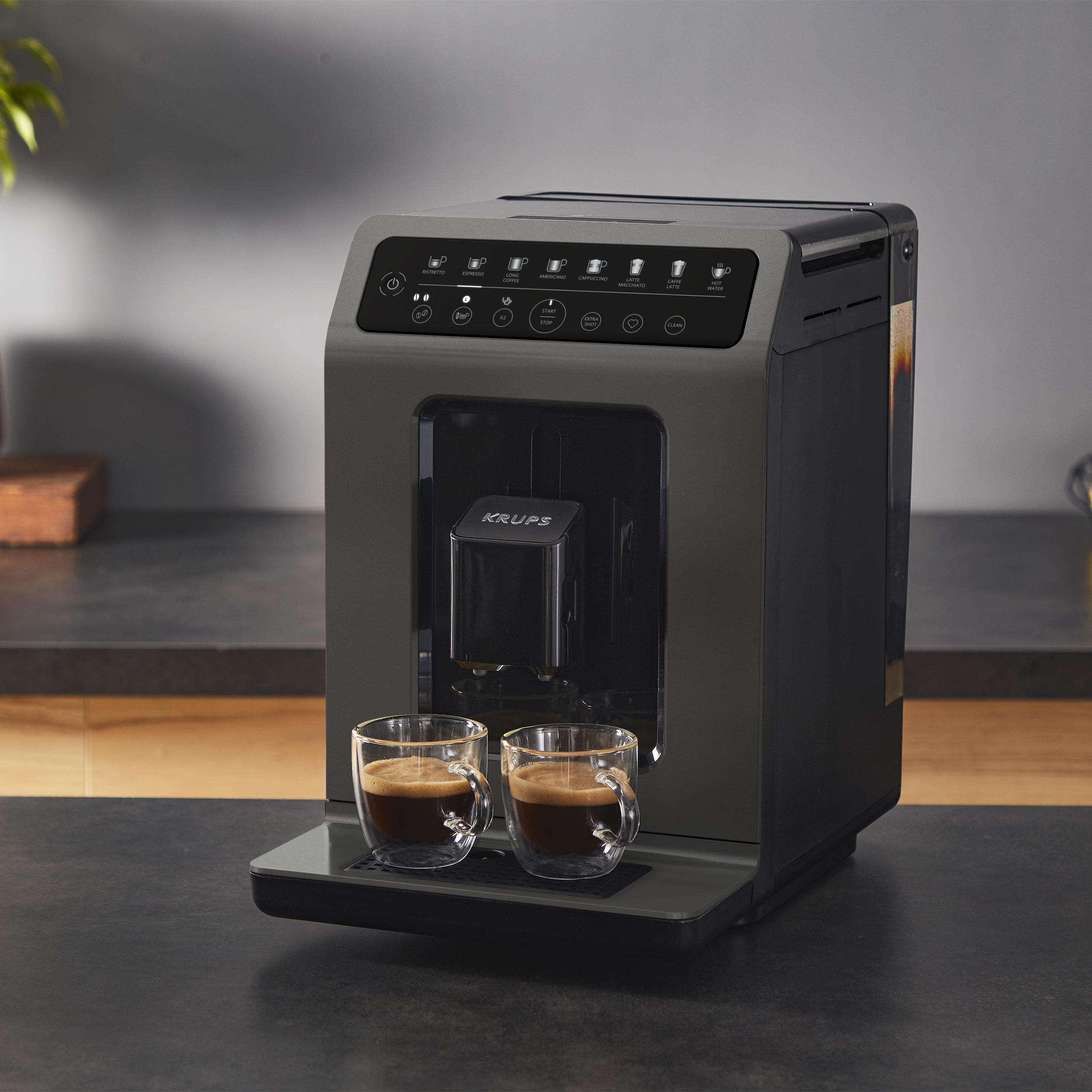 Eine dunkelgraue Kaffeemaschine mit zwei Glasbechern Espresso auf einer Arbeitsplatte.