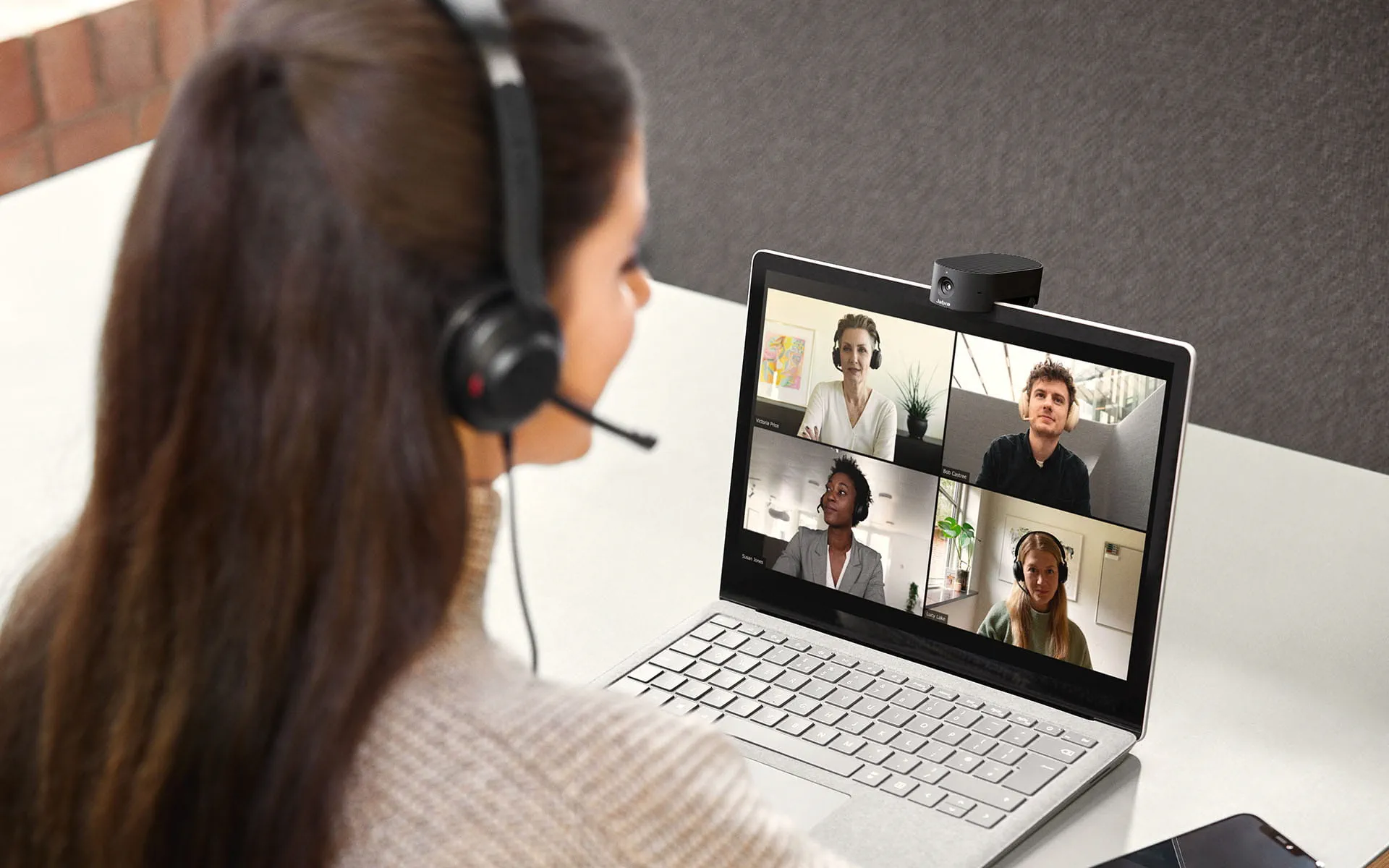Frau benutzt einen Laptop mit einer Webcam oben, Videokonferenz mit anderen Personen auf dem Bildschirm.