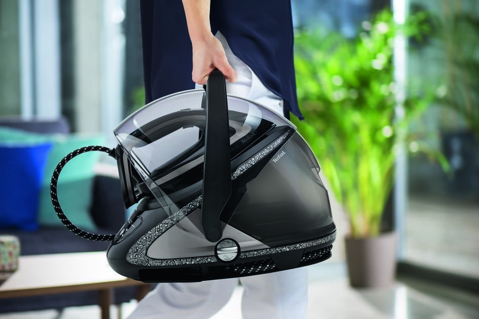 Osoba trzymająca czarno-srebrne żelazko, z jasnym tłem.