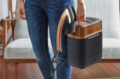 Osoba trzymająca czarne i brązowe żelazko parowe i jego podstawę.