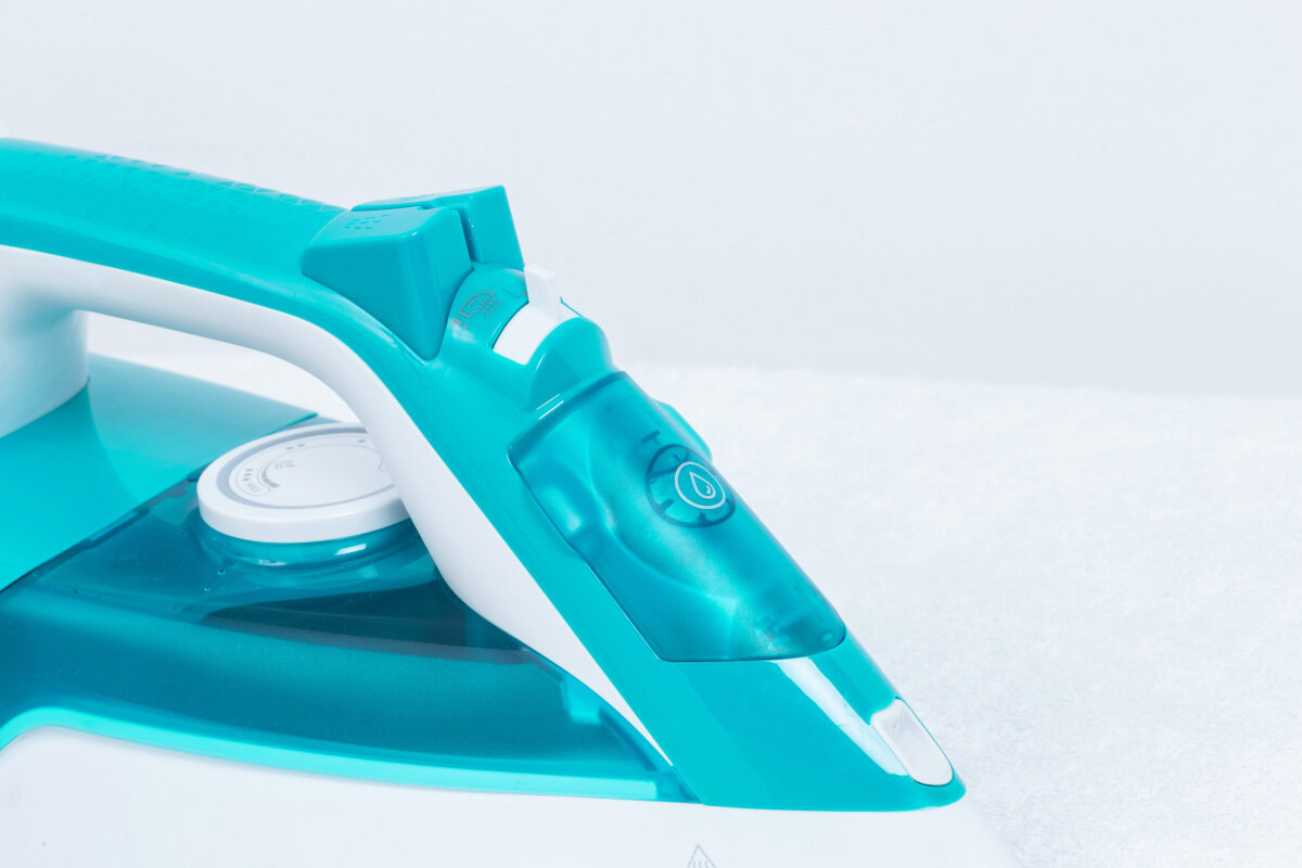 Zbliżenie turkusowo-białego żelazka z uchwytem i korkiem do napełniania wodą.