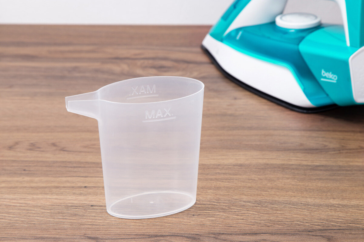 Przezroczysta plastikowa miarka z dzióbkiem. W tle żelazko.