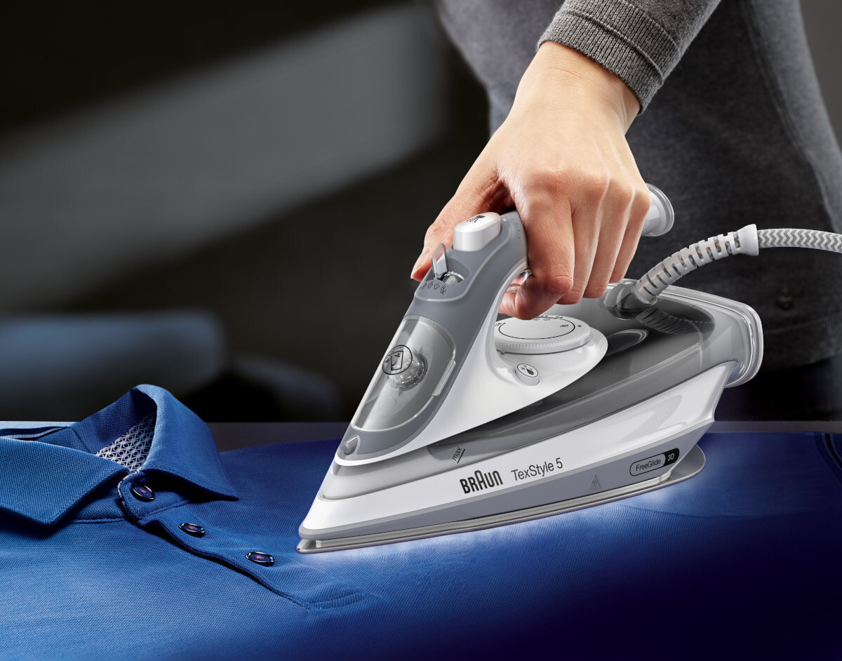 Osoba prasująca niebieską koszulkę polo szaro-białym żelazkiem.