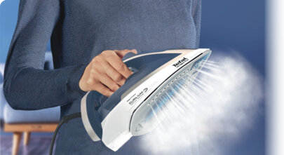 Osoba prasuje żelazkiem Tefal, z którego wydobywa się para. Niebieska ściana w tle.