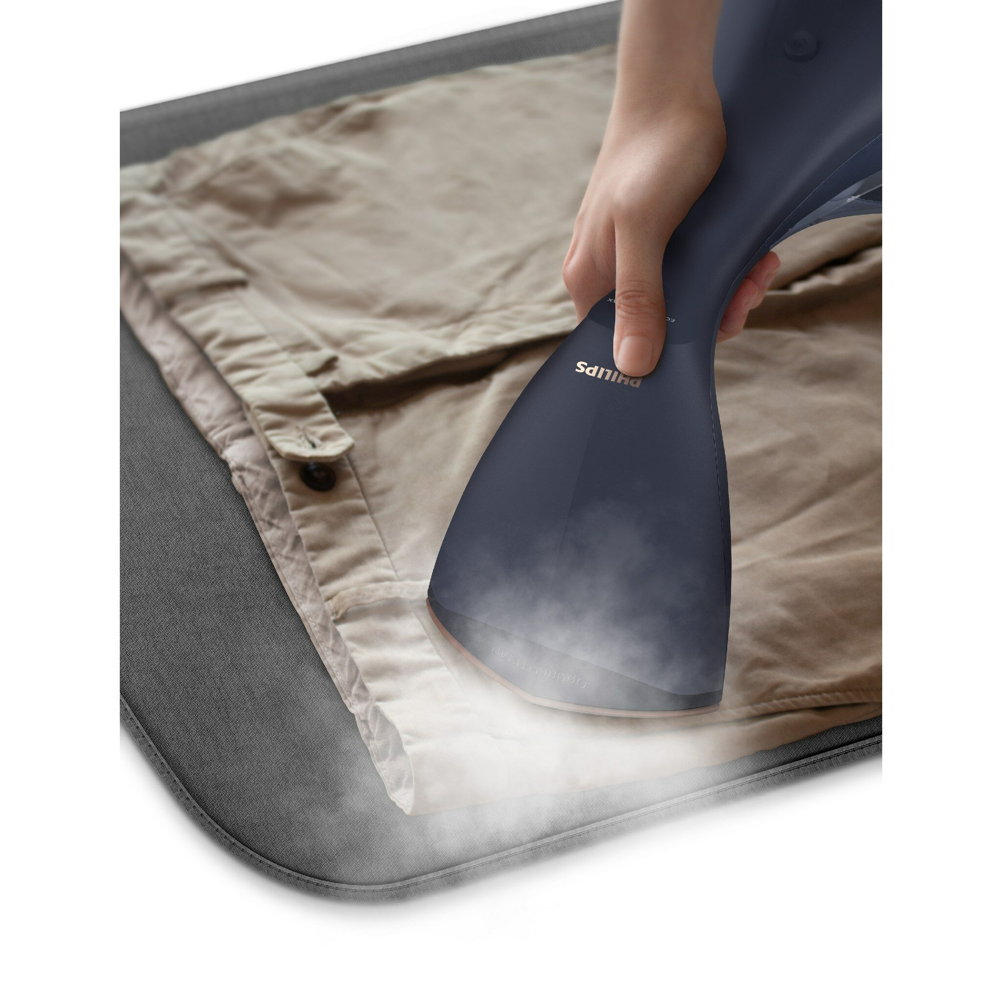 Ręka używa granatowej parownicy Philips na beżowej koszuli, widoczna para. Na szarej powierzchni.