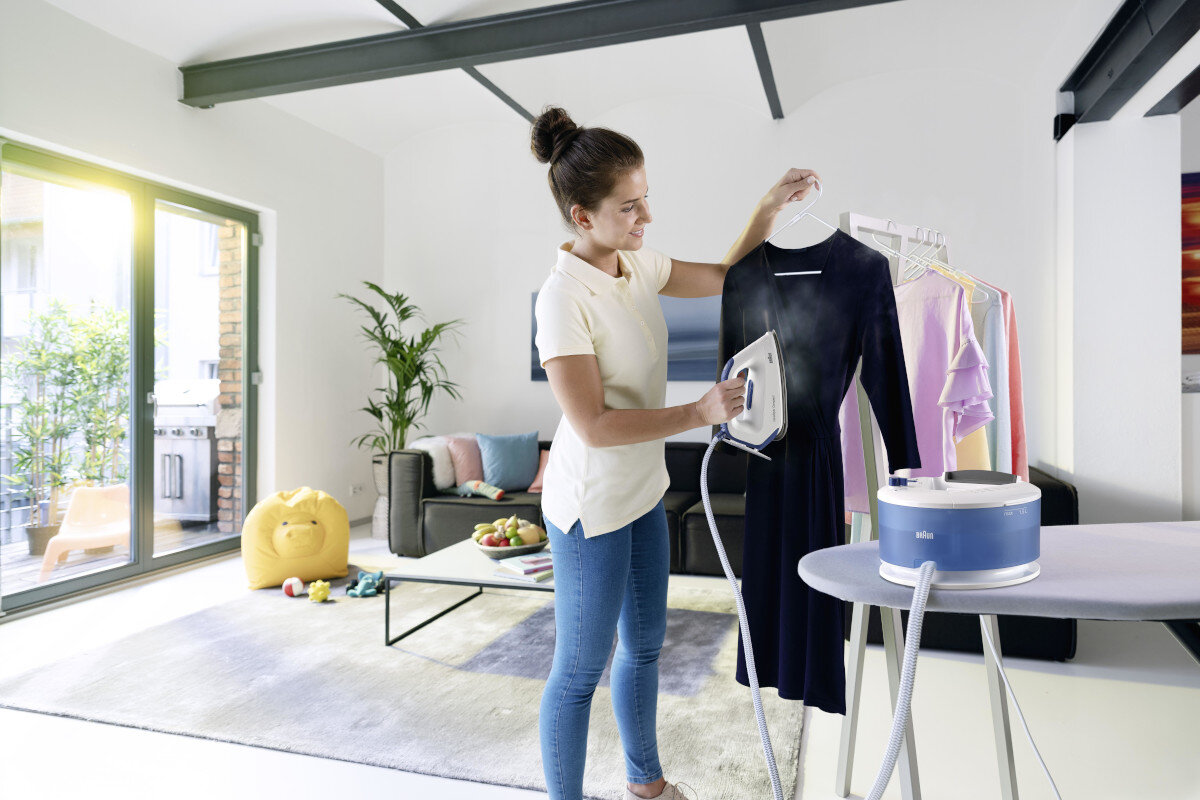 Kobieta prasująca czarną sukienkę na desce do prasowania. Para jest widoczna.