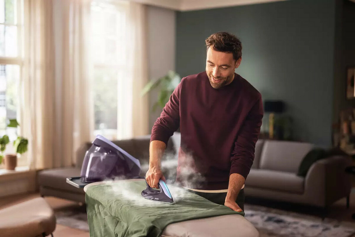 Mężczyzna prasujący zielony element garderoby na desce do prasowania z parą.