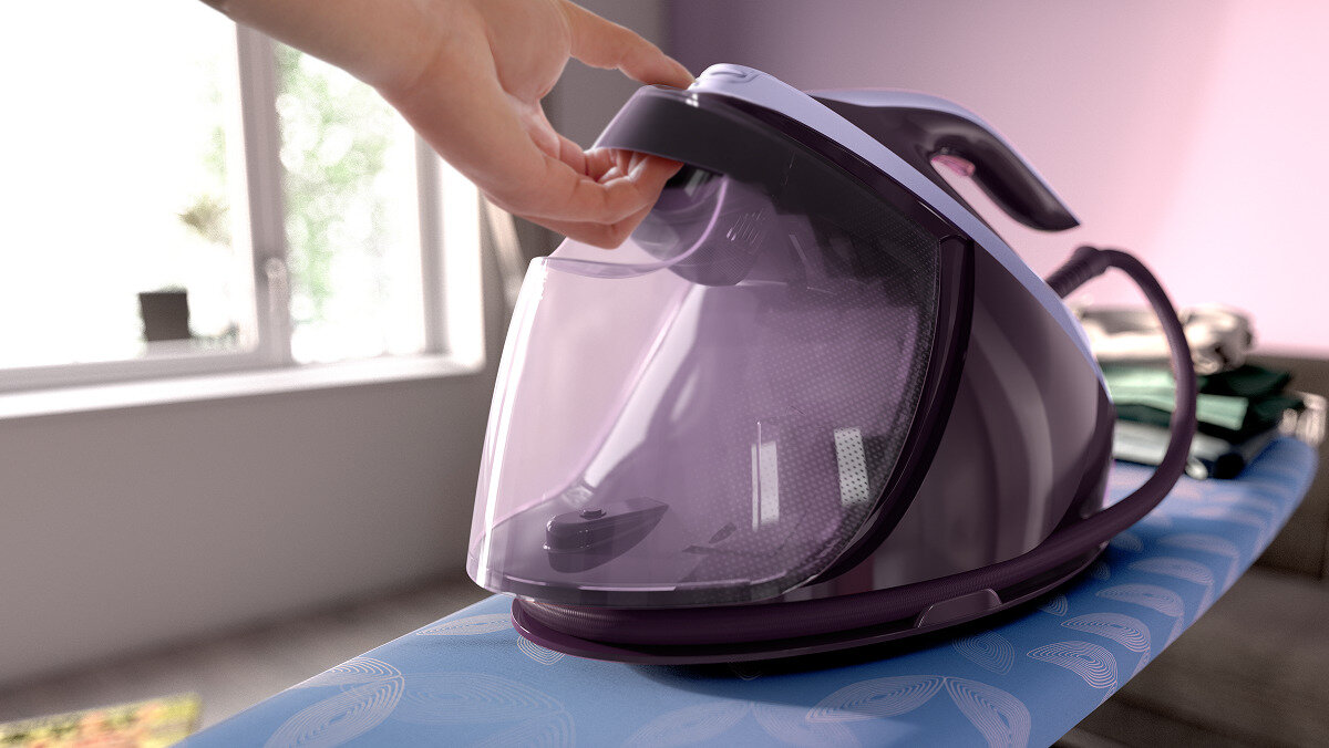 Ręka otwierająca zbiornik na wodę fioletowego żelazka na desce do prasowania. Ubrania na desce.