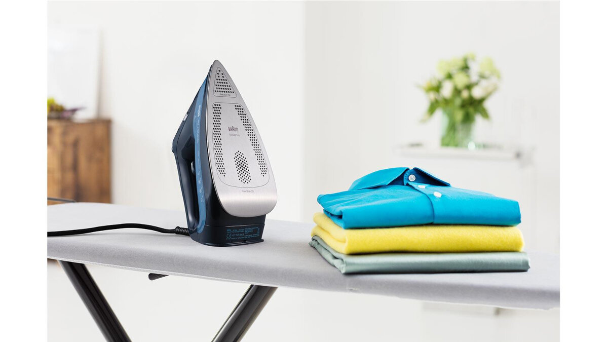 Deska do prasowania z żelazkiem i złożonymi koszulami, kwiaty w tle.