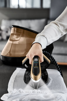 Osoba prasuje białą koszulę żelazkiem parowym na stole.