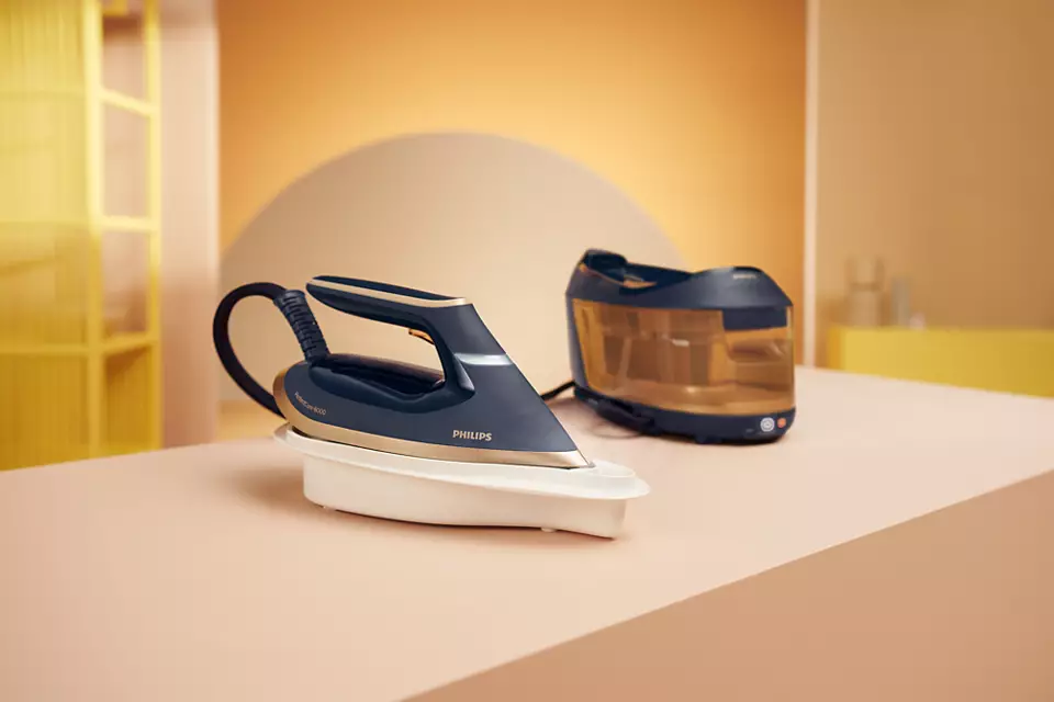 Żelazko z generatorem pary, oba w kolorze niebieskim i złotym, na różowej powierzchni.