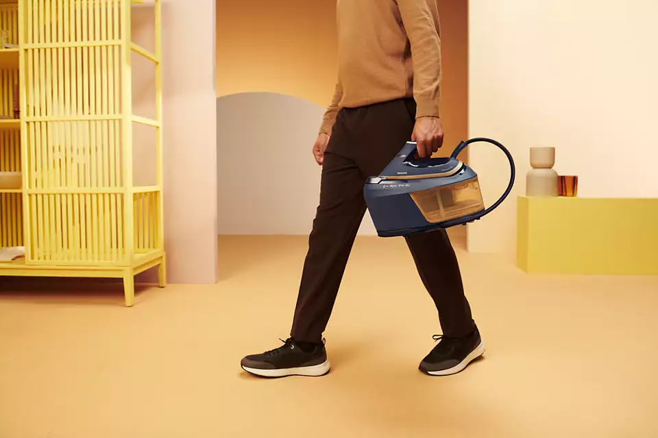 Mężczyzna w beżowym swetrze trzyma niebieski generator pary w jasnym pokoju.