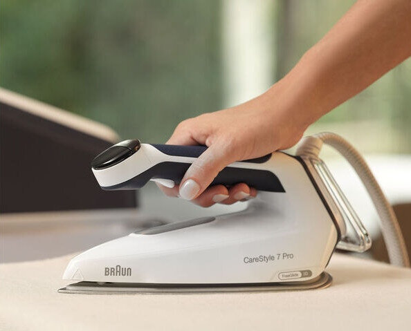 Dłoń trzymająca biało-niebieskie żelazko nad stołem.