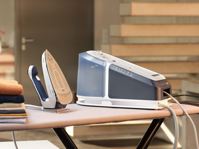 Stacja do prasowania z generatorem pary, żelazkiem i deską do prasowania. Stos ubrań po lewej.