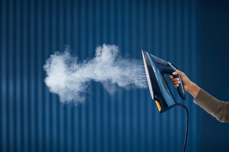 Osoba prasuje czarnym żelazkiem, para wydobywa się na niebieskim paskowanym tle.