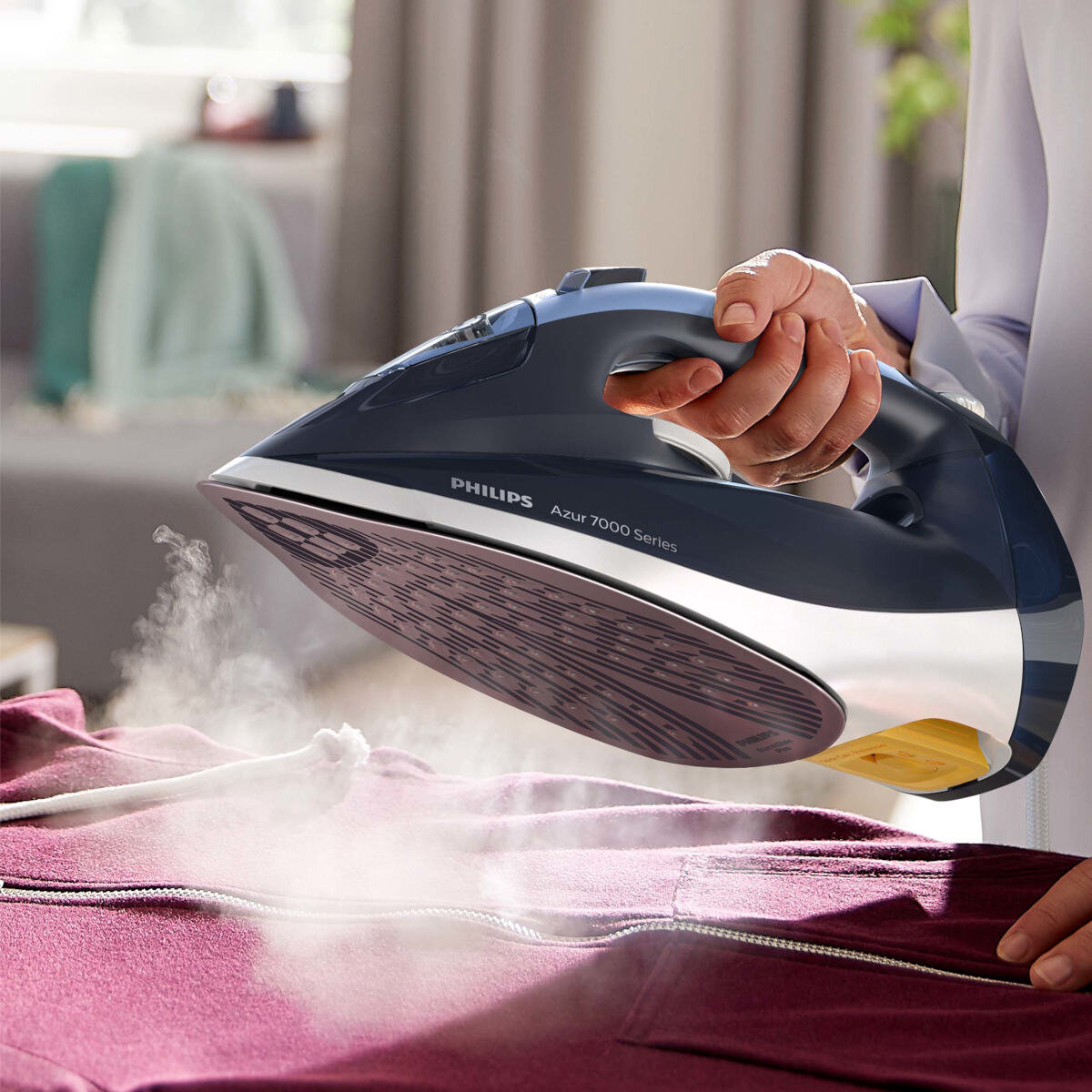 Osoba prasuje fioletową kurtkę żelazkiem Philips. Para jest widoczna. Żelazko jest niebiesko-białe.
