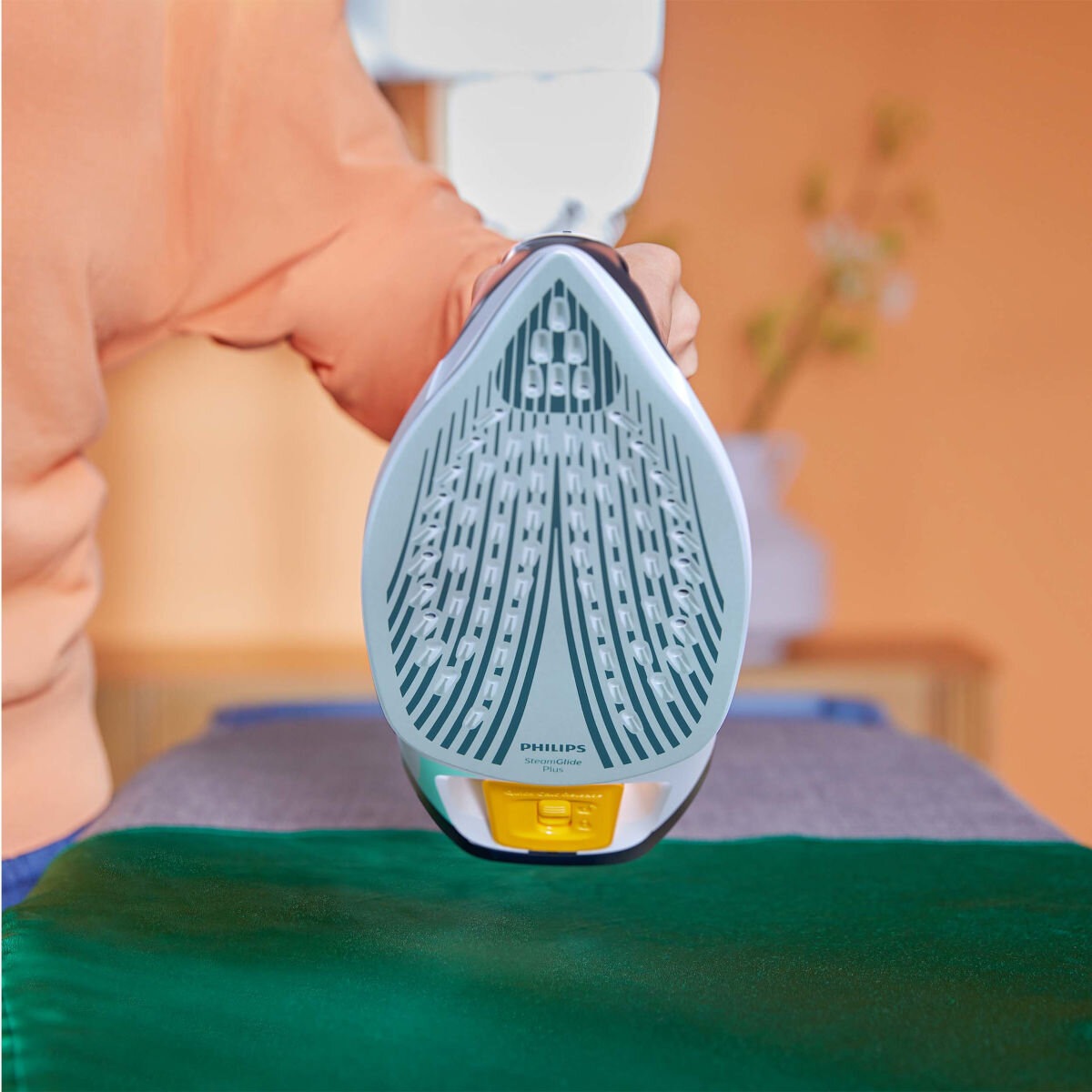 Osoba trzymająca żelazko Philips nad zieloną tkaniną. Żelazko jest szare i białe.