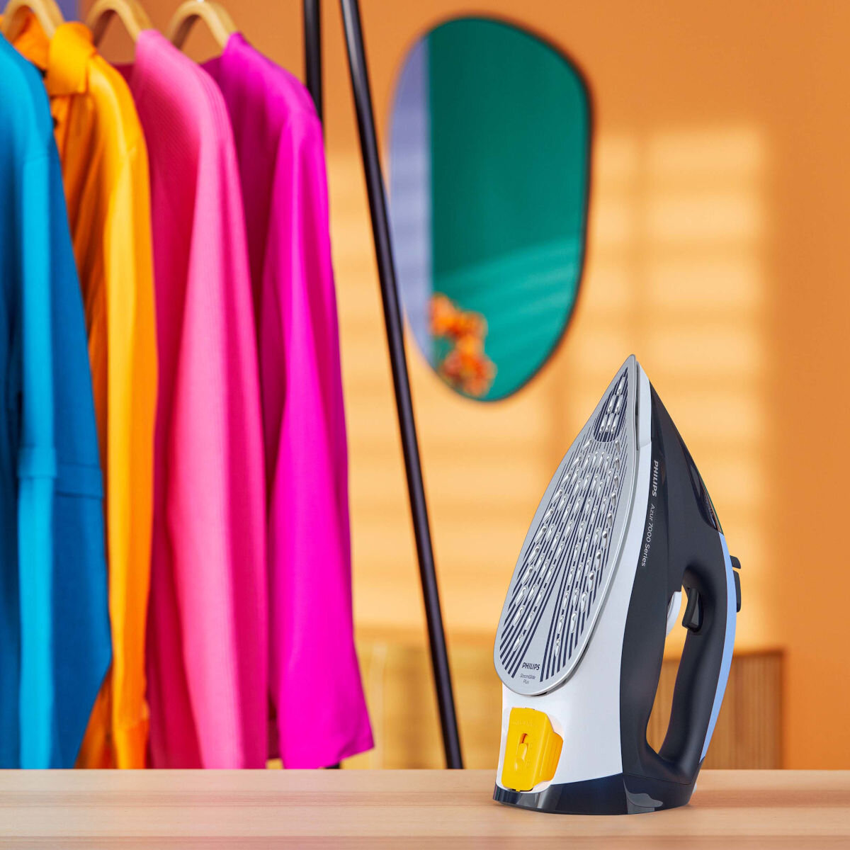 Żelazko Philips na stole z ubraniami i lustrem w tle.