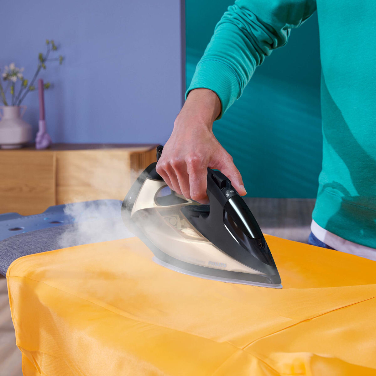 Osoba prasująca żółtą tkaninę czarnym żelazkiem.