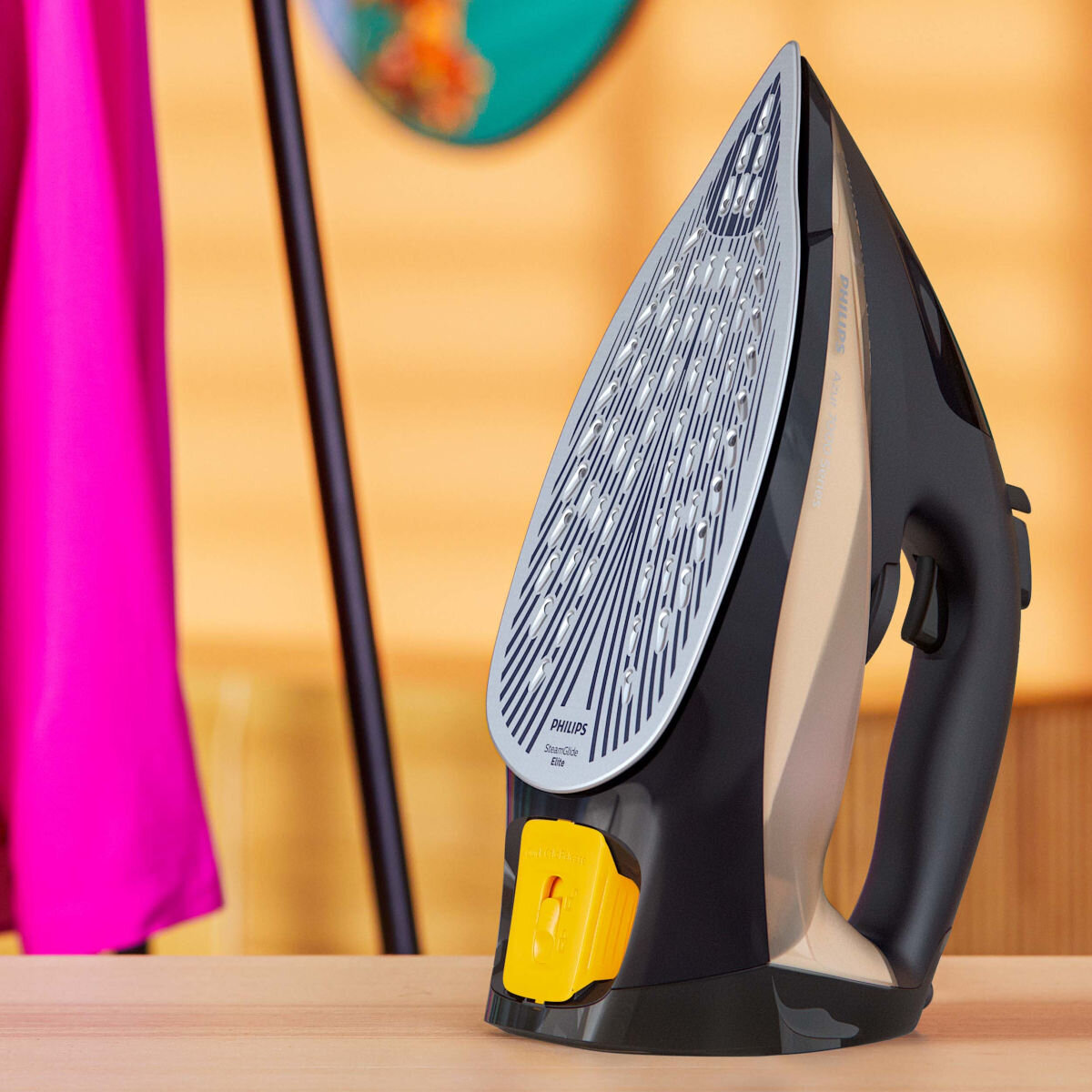 Czarne i złote żelazko na drewnianym stole. Różowa tkanina w tle.