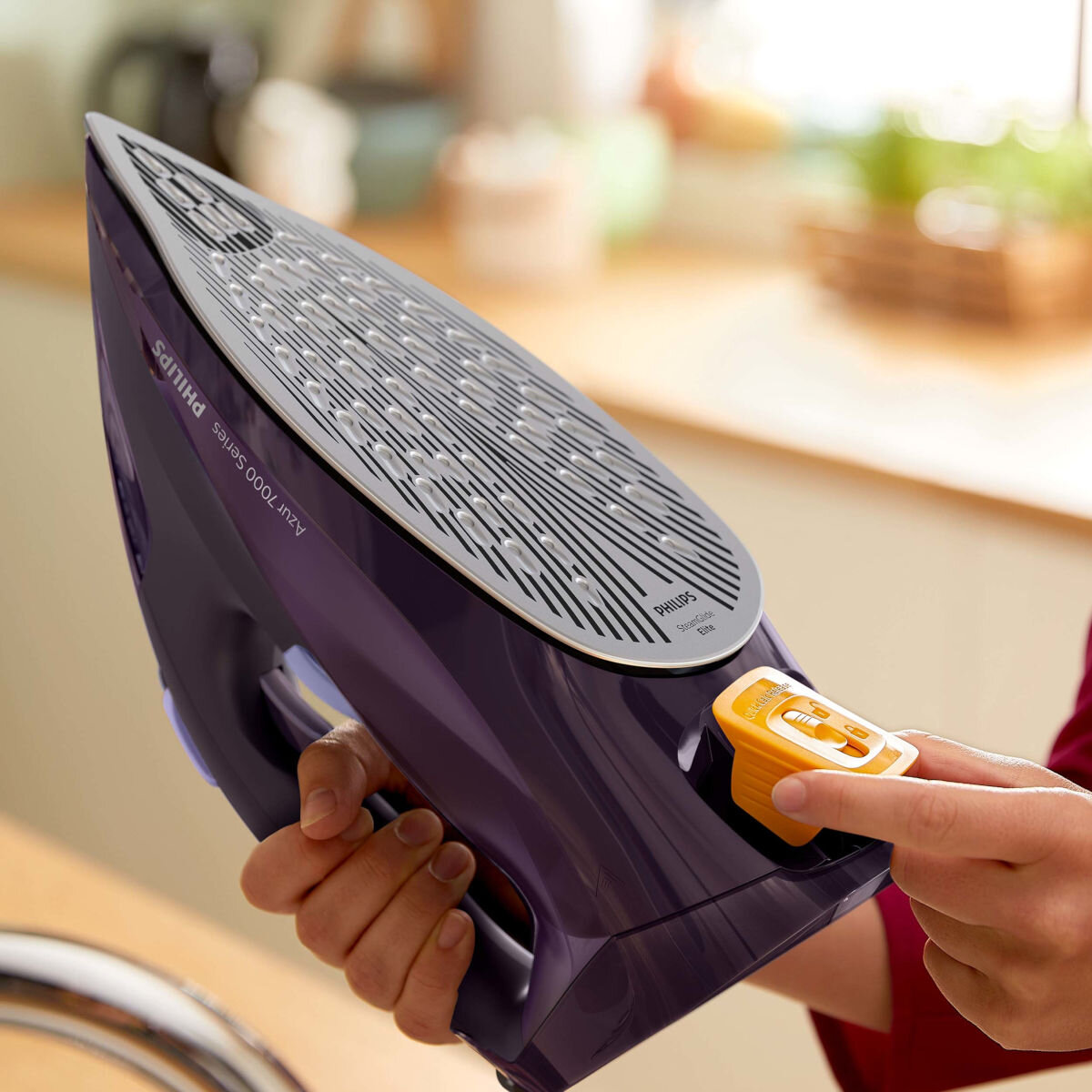 Osoba trzymająca fioletowe żelazko. Żelazko jest z bliska, a osoba w rogu.