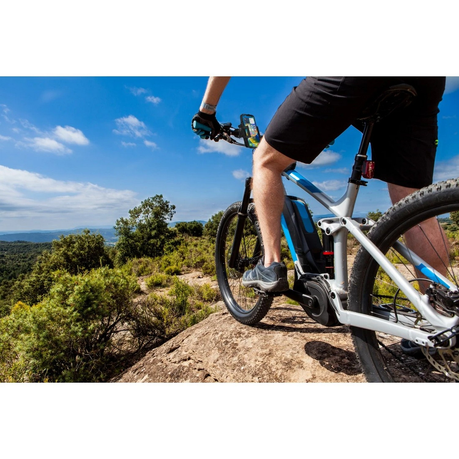 Personne faisant du vélo électrique sur un sentier rocheux sous un ciel bleu avec des arbres.