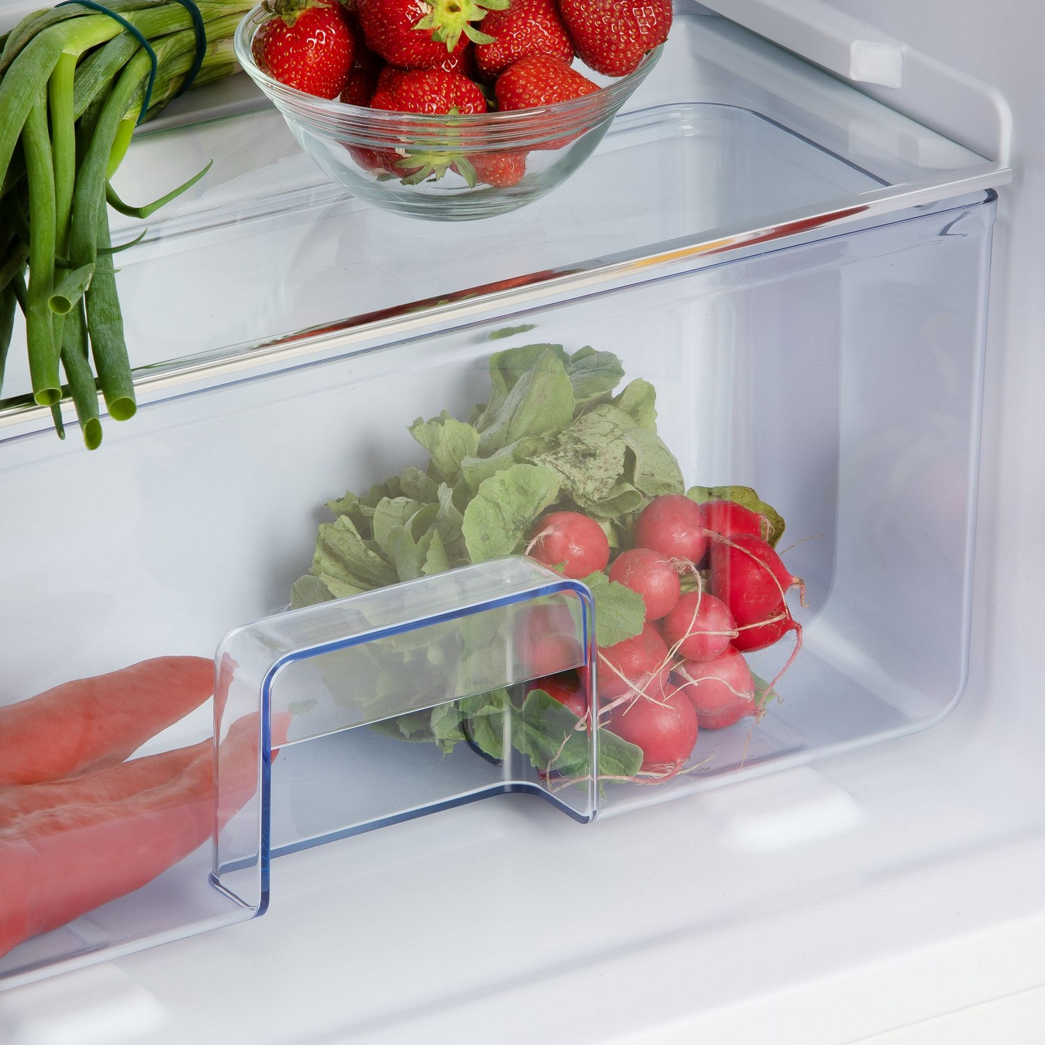 Refrigerator drawer with vegetables: radishes, scallions, and lettuce. Hand reaches in.