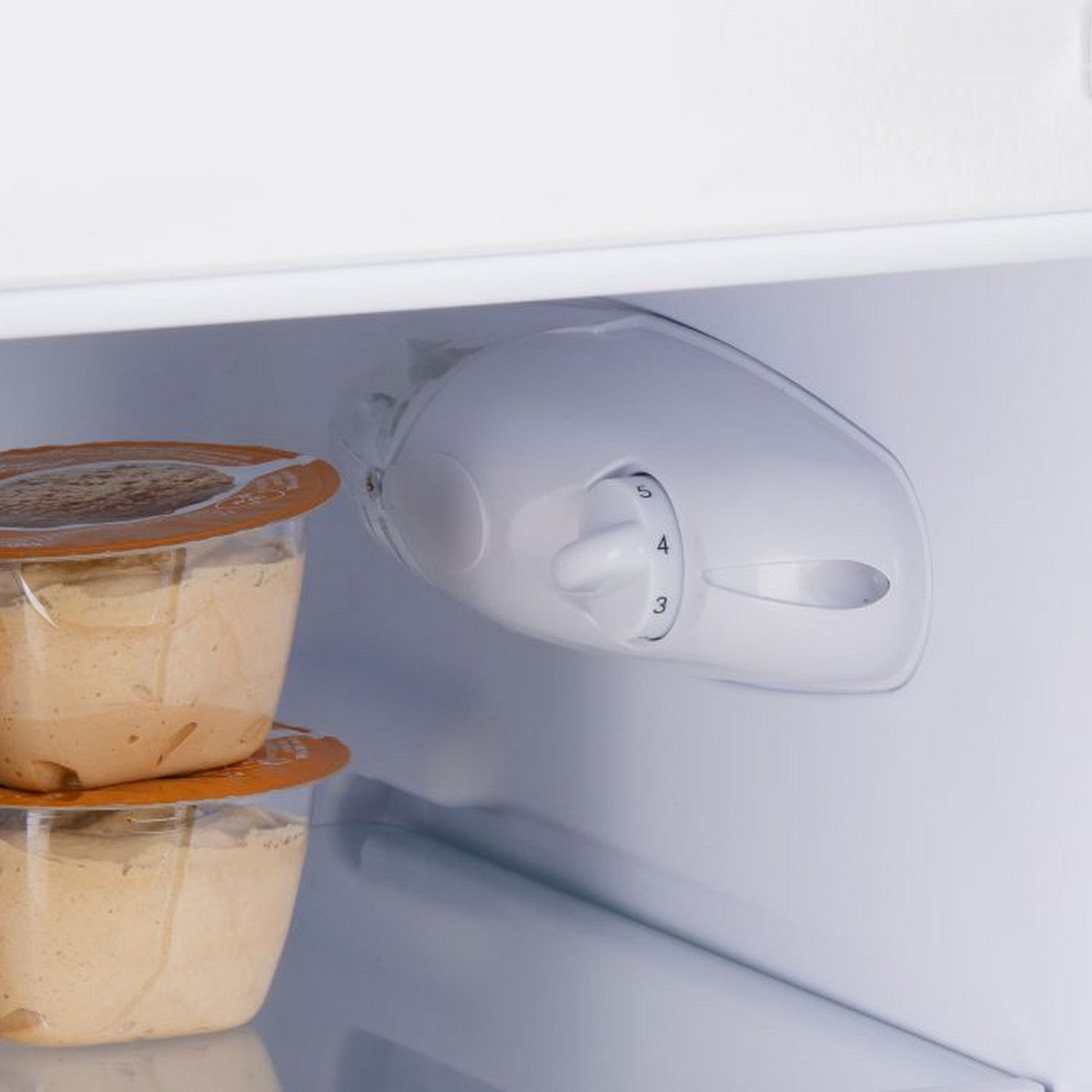 Intérieur du réfrigérateur avec une molette de contrôle de la température et des contenants alimentaires.
