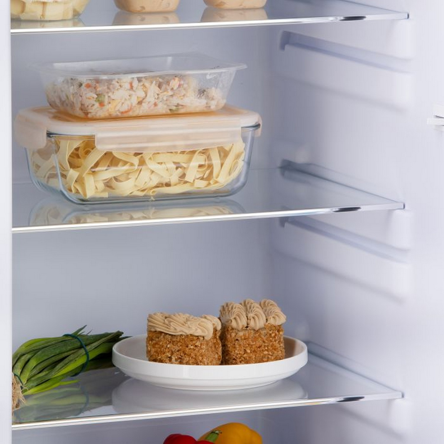 Étagères de réfrigérateur avec des boîtes alimentaires et des gâteaux. Oignons verts à gauche. Intérieur blanc.