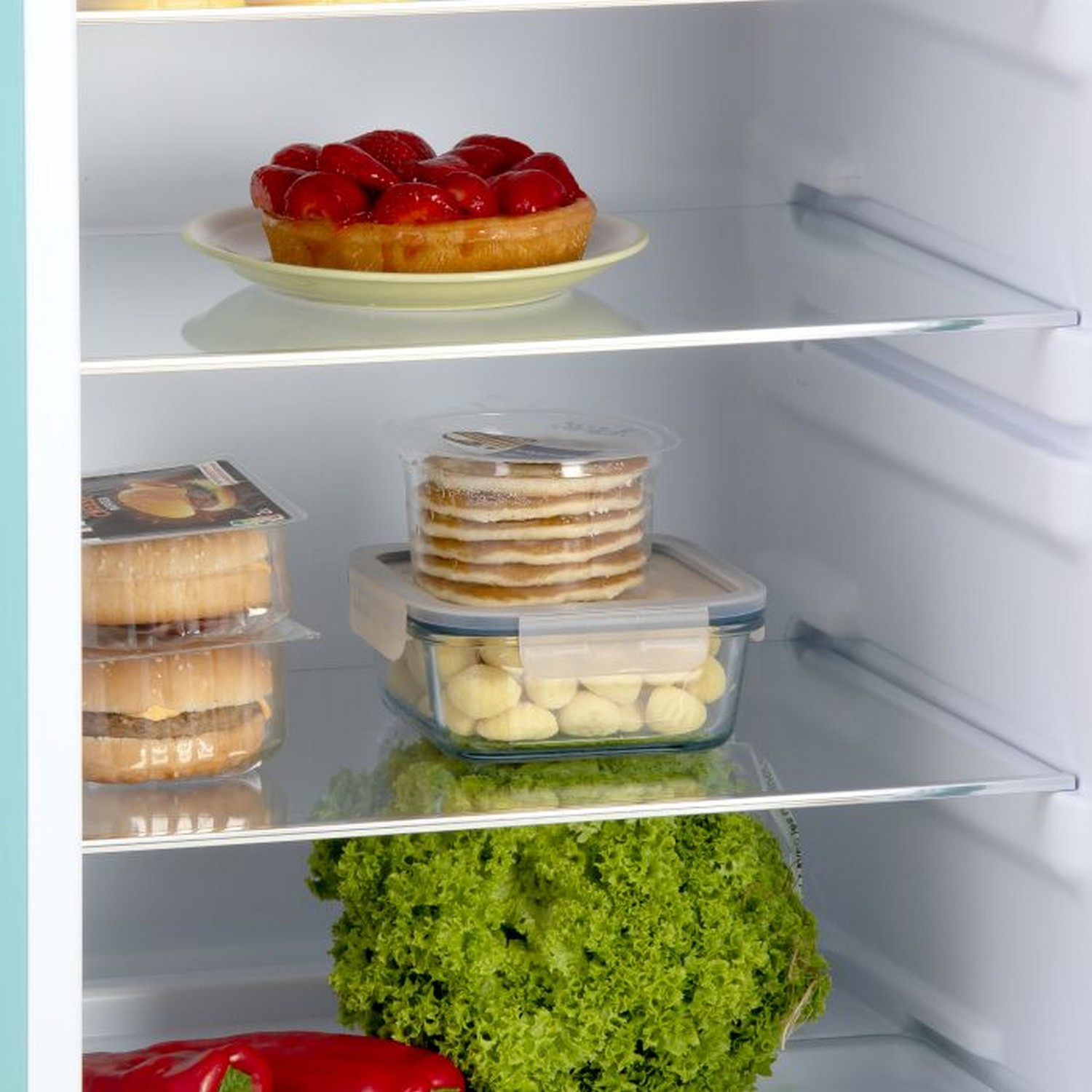 Intérieur de réfrigérateur avec de la nourriture. Fraises, crêpes, salade et autres aliments.