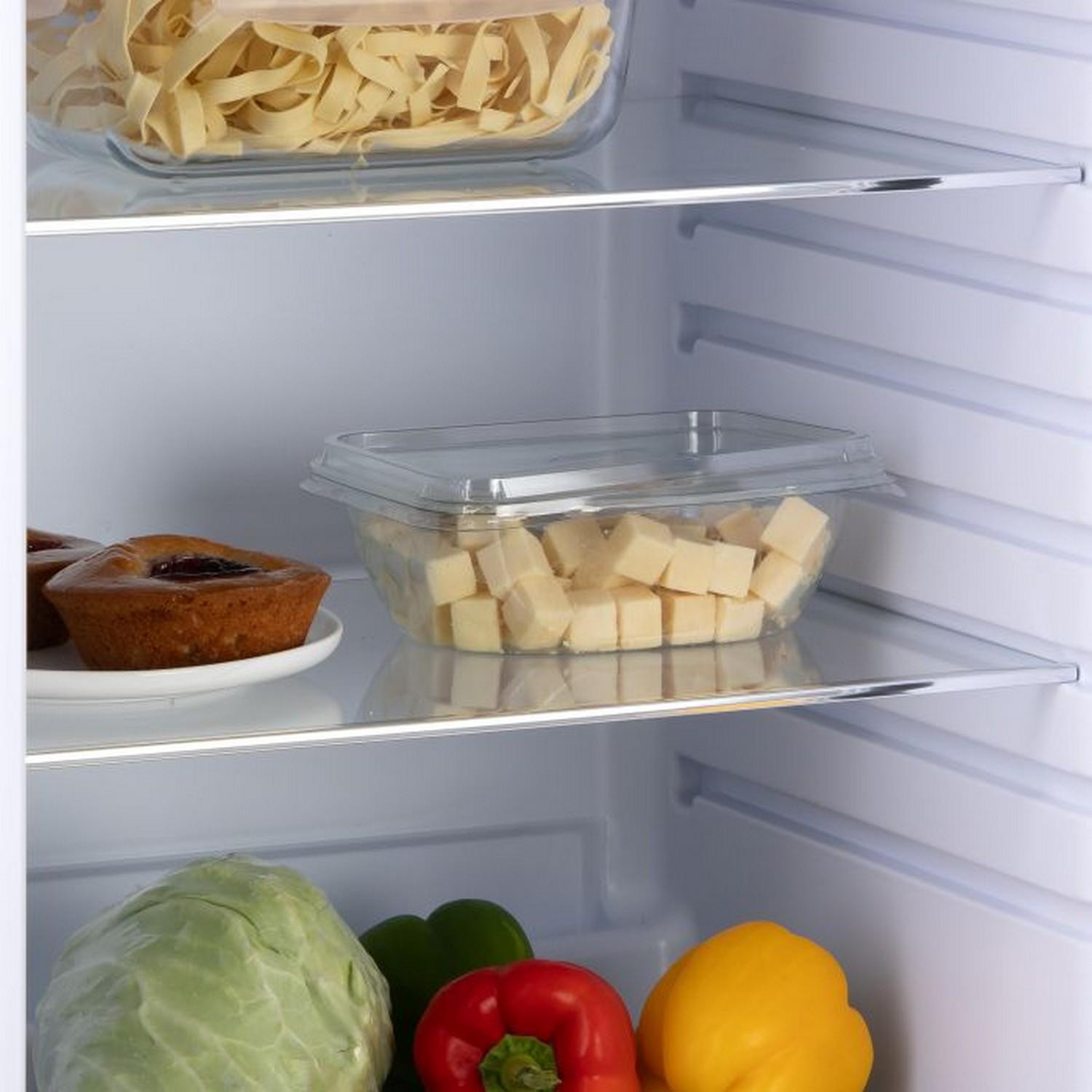 Intérieur du réfrigérateur : pâtes, cubes de fromage, muffins, chou, poivrons.