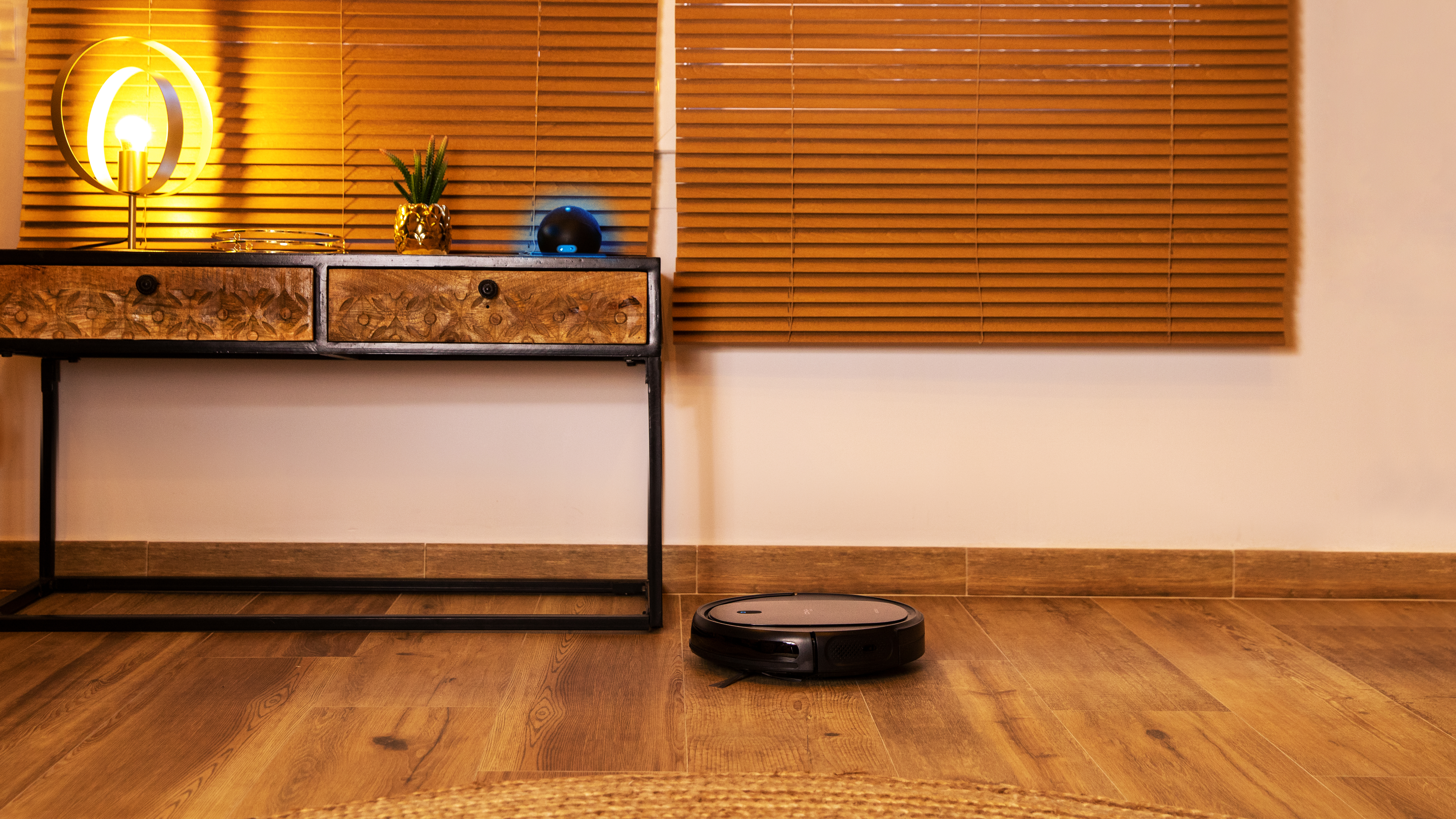 Una habitación con un robot aspirador en un suelo de madera, cerca de una alfombra.