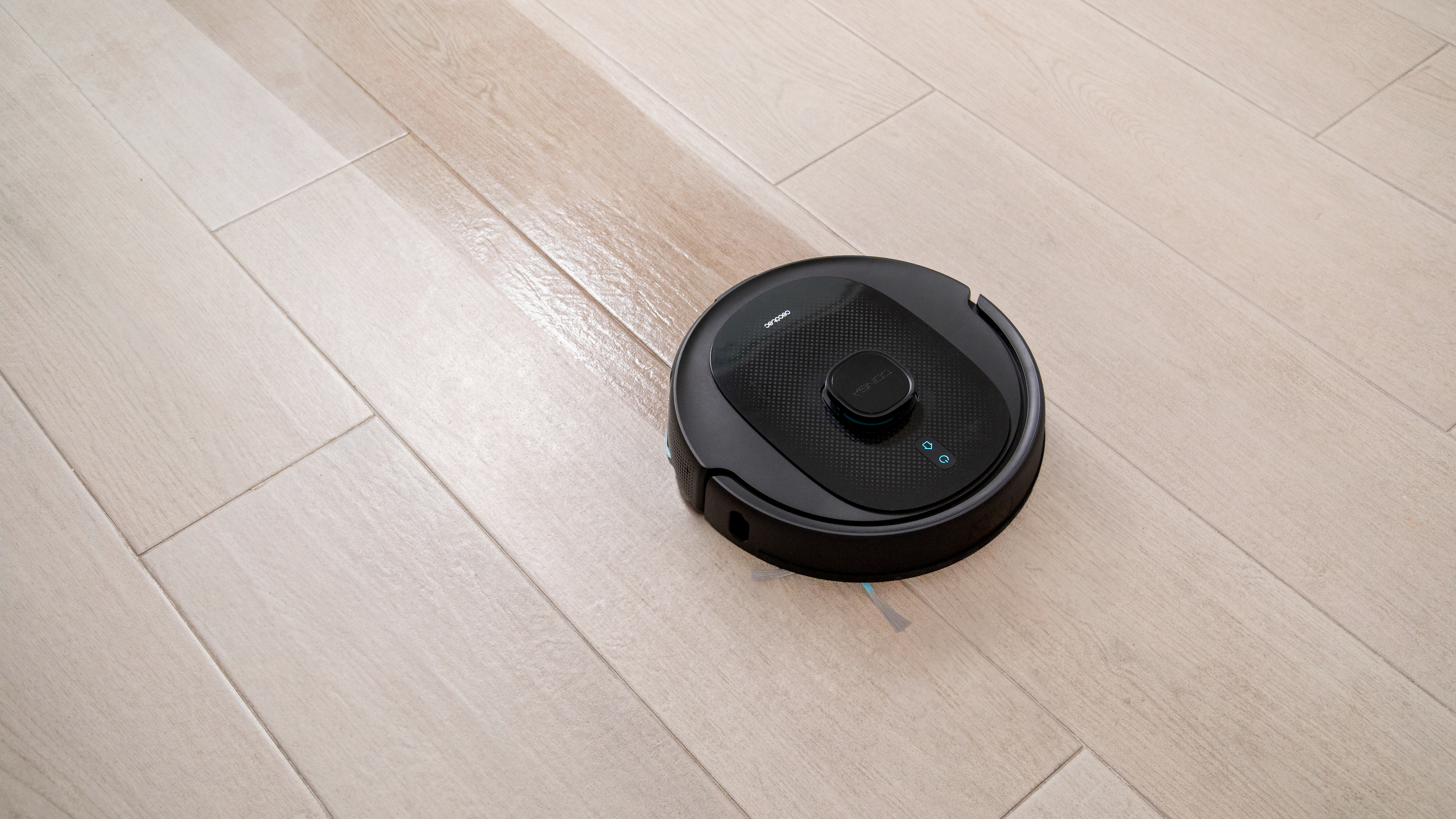 Una aspiradora robot negra en un suelo de madera clara. El suelo está limpio.