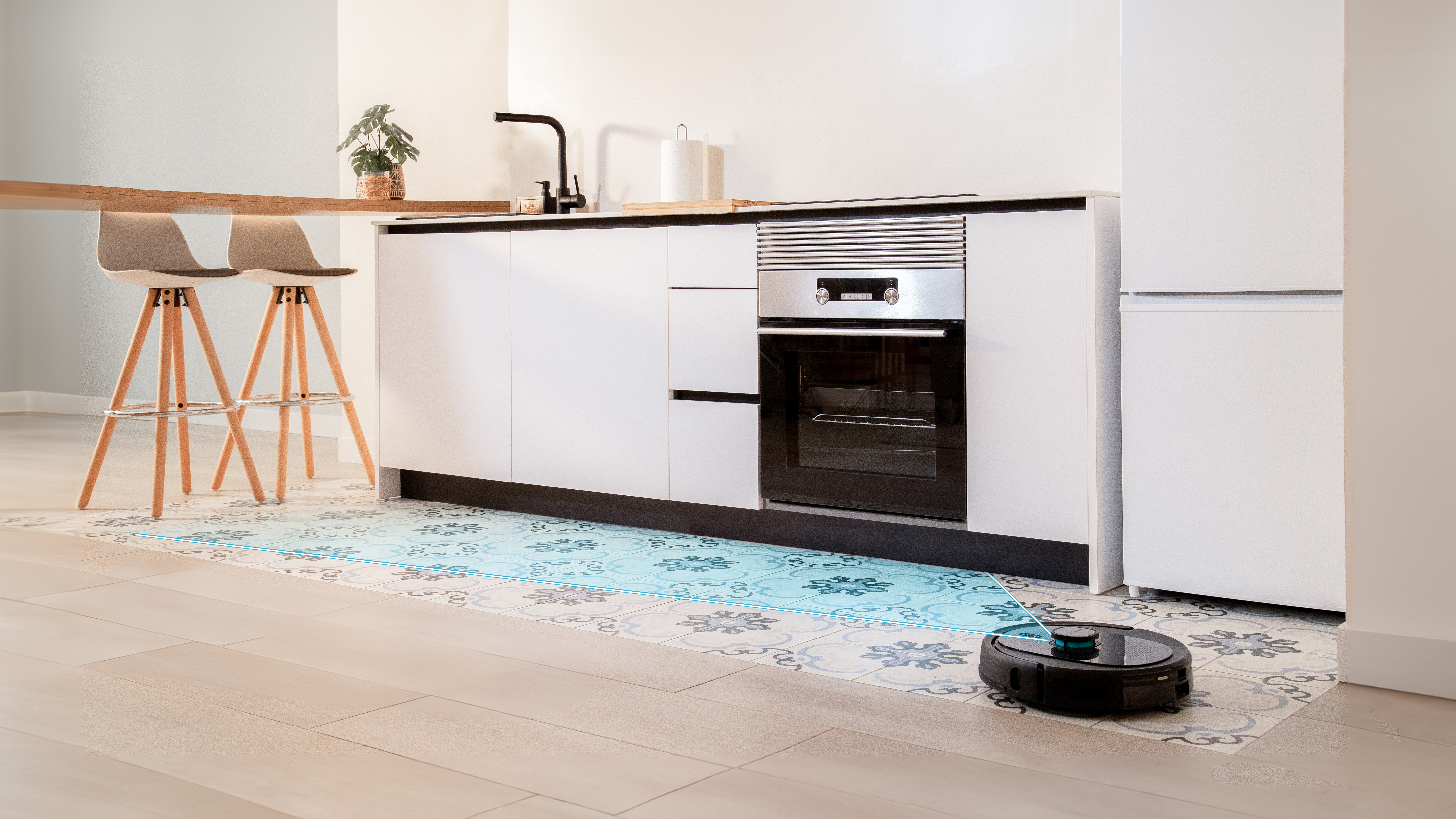 Un robot aspirador limpiando el suelo de una cocina con un diseño de baldosas.