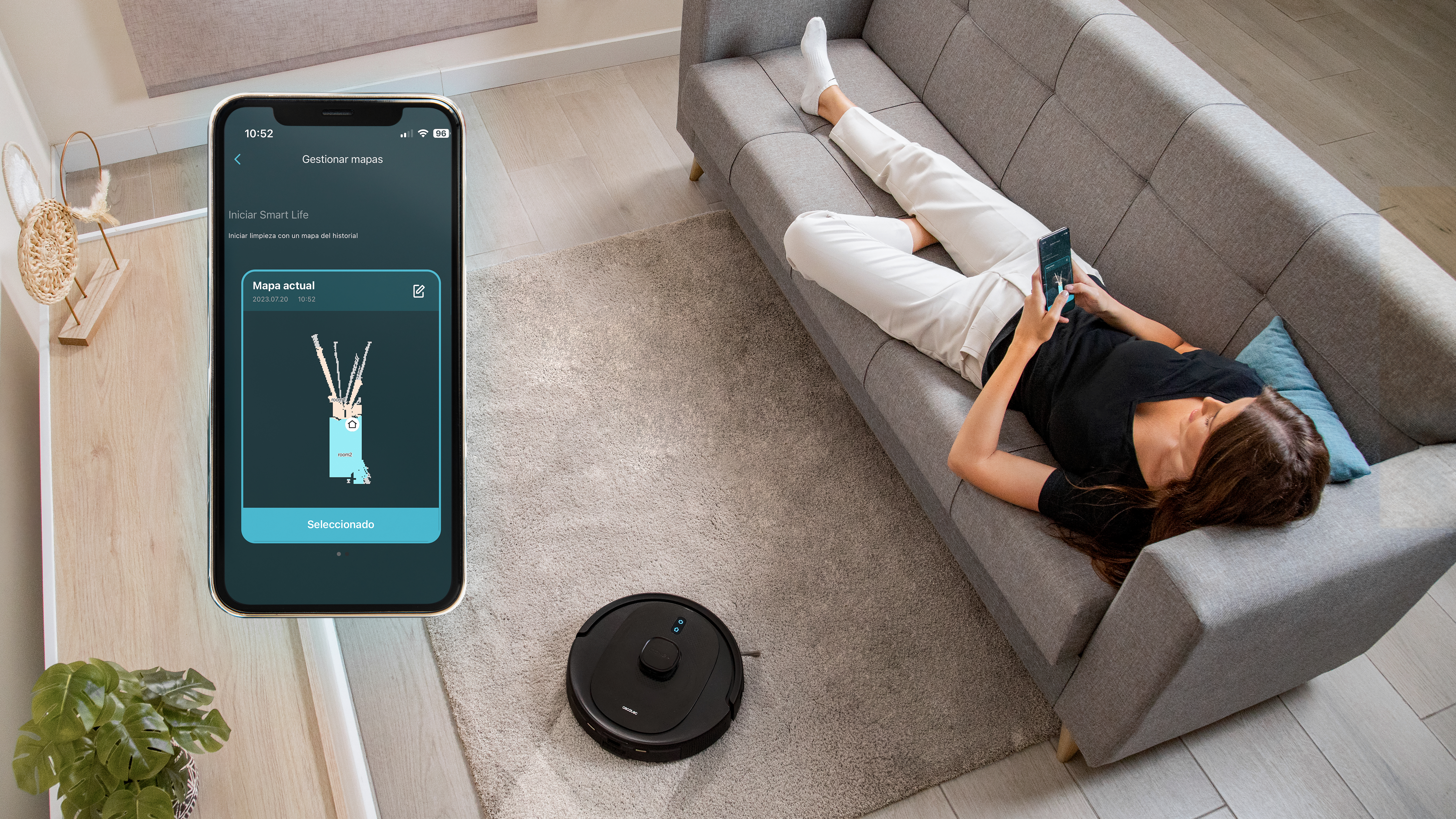 Mujer en sofá usando teléfono, mientras el robot aspirador limpia. Interior de habitación.