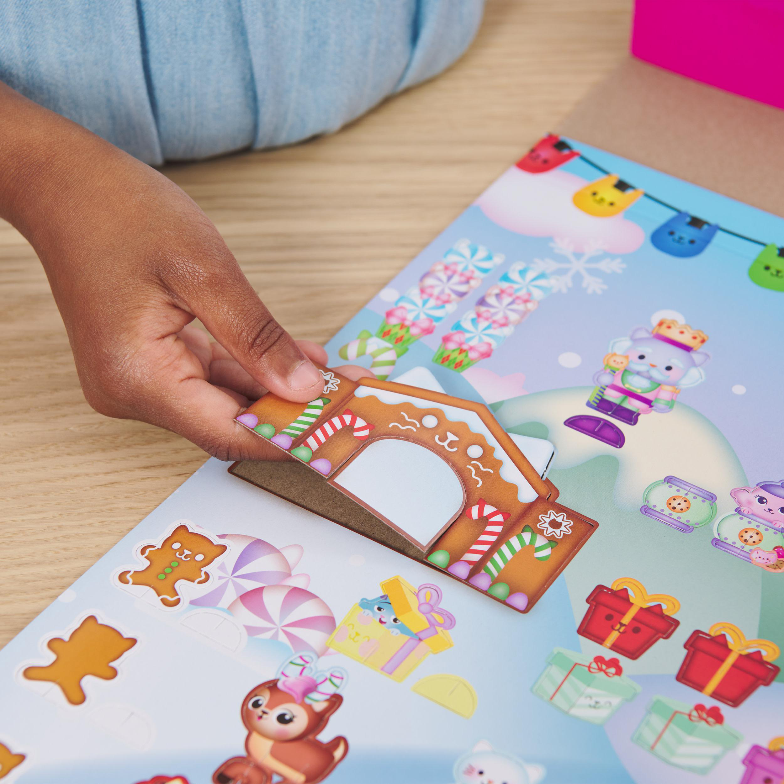 Eine Hand, die einen Lebkuchenhaus-Aufkleber auf ein weihnachtliches Stickerbogen klebt.
