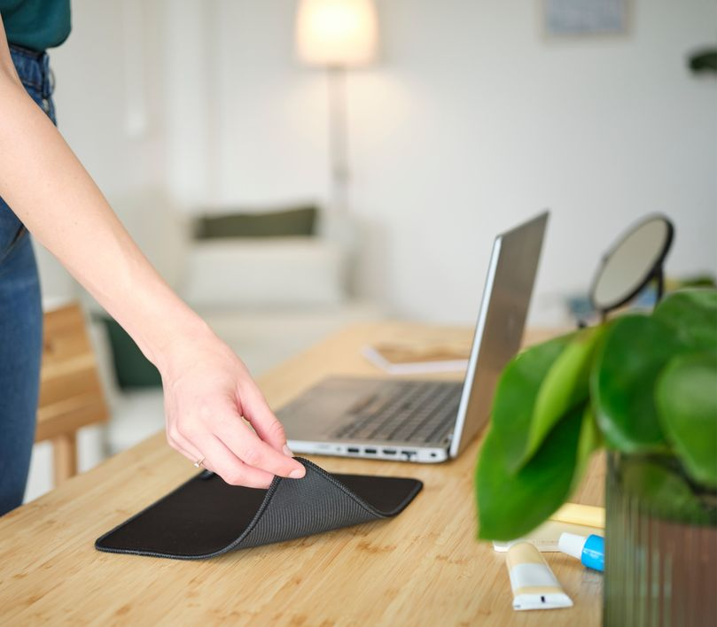 Egy személy keze fekete egérpadot helyez egy fa asztalra egy laptop mellé.