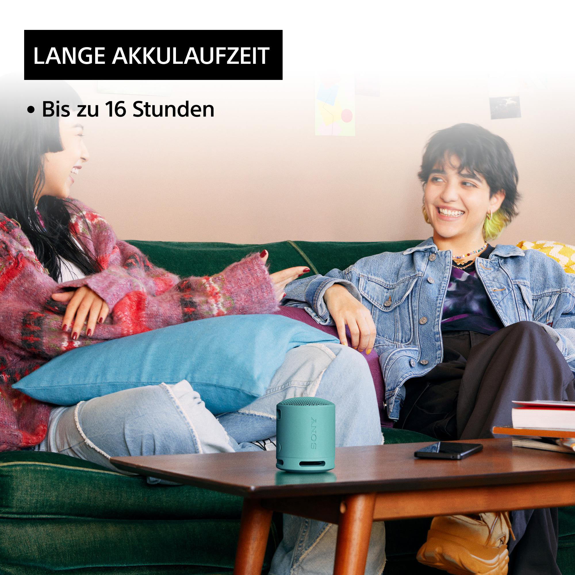 Zwei lächelnde Frauen, eine hält einen Lautsprecher in einem Raum.