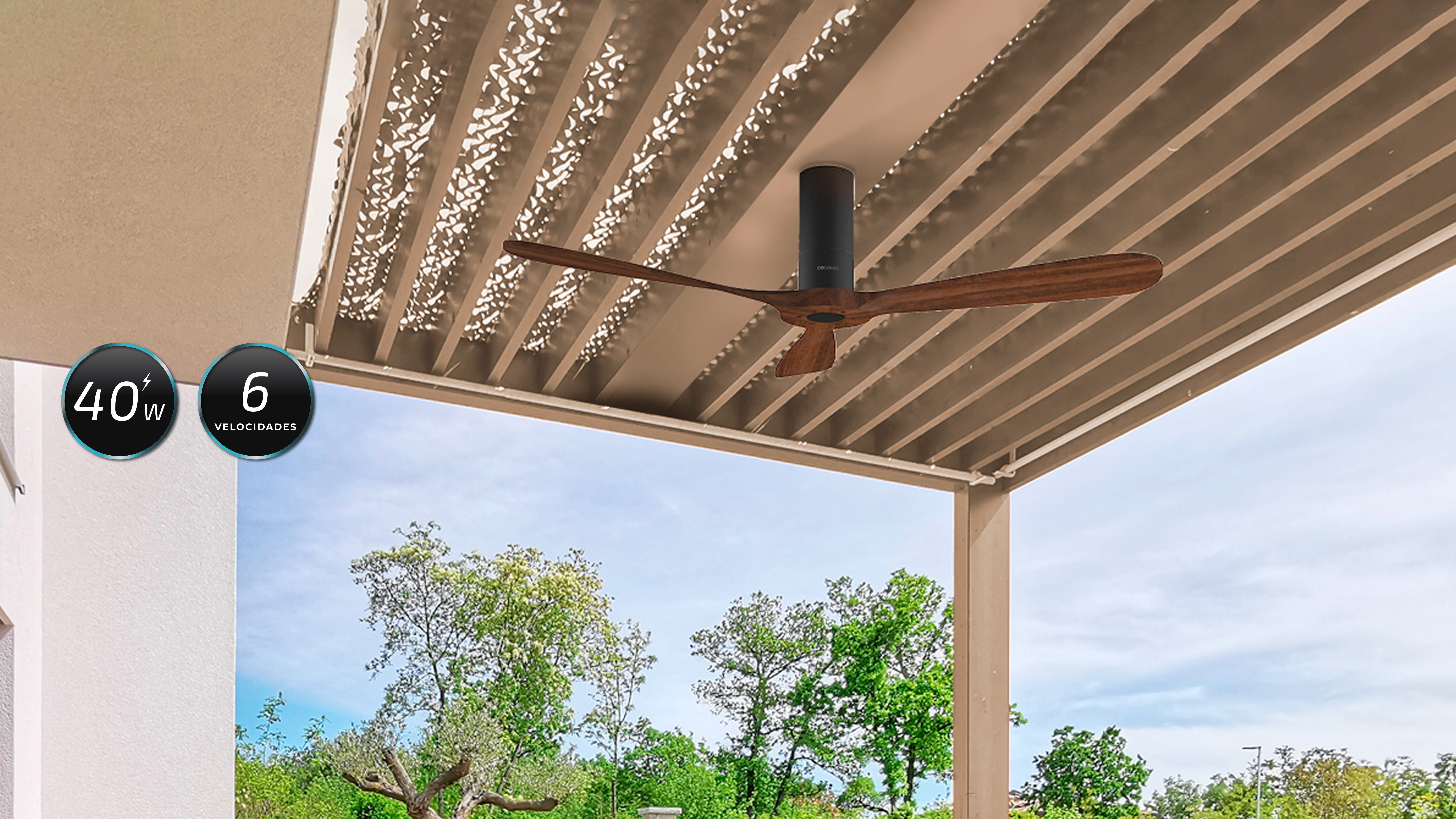 Ventilador de techo exterior con aspas de madera. Árboles verdes y cielo visibles. Construcción gris y blanca.