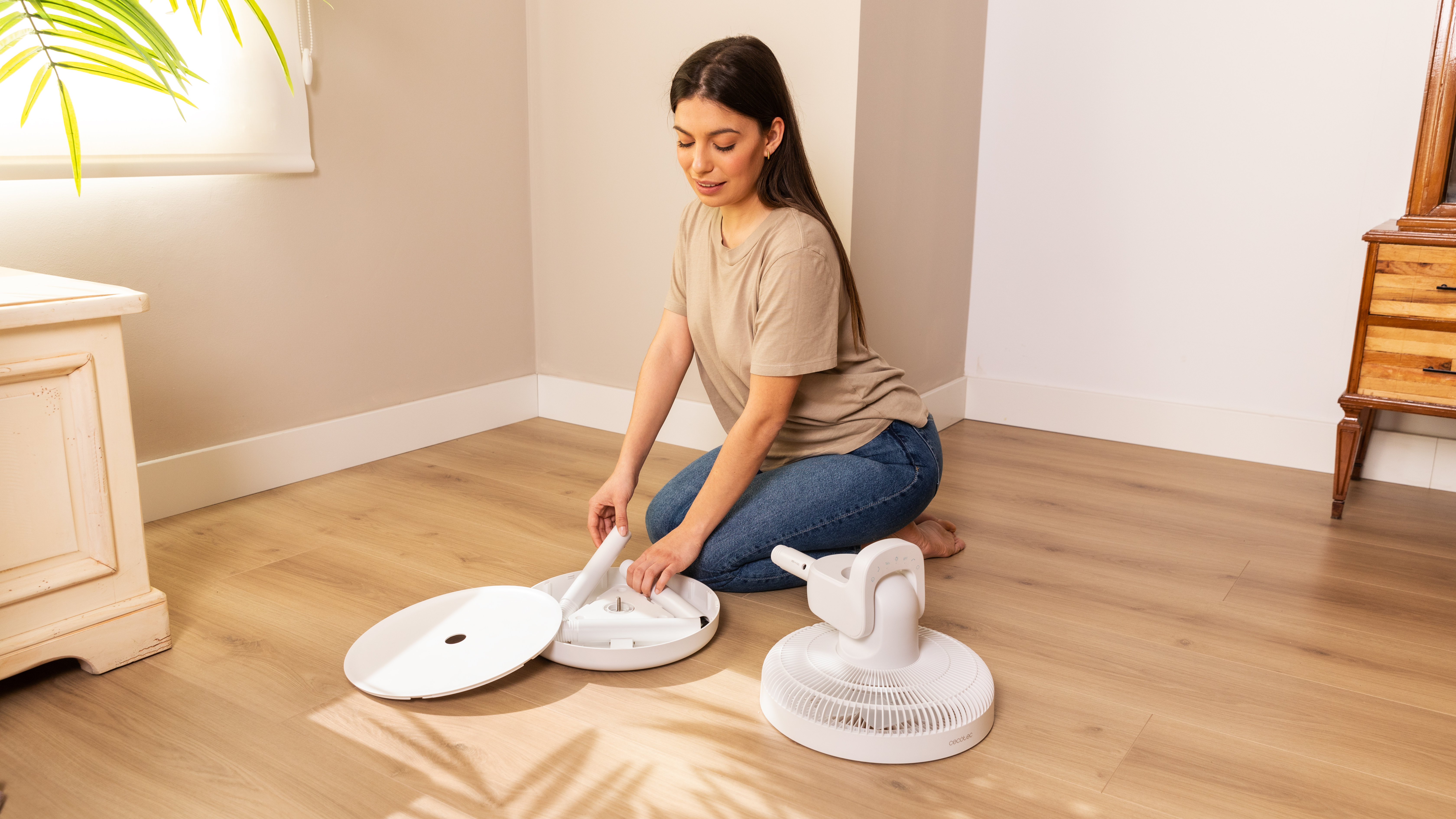Una mujer montando un ventilador blanco en un suelo de madera, con las piezas delante.
