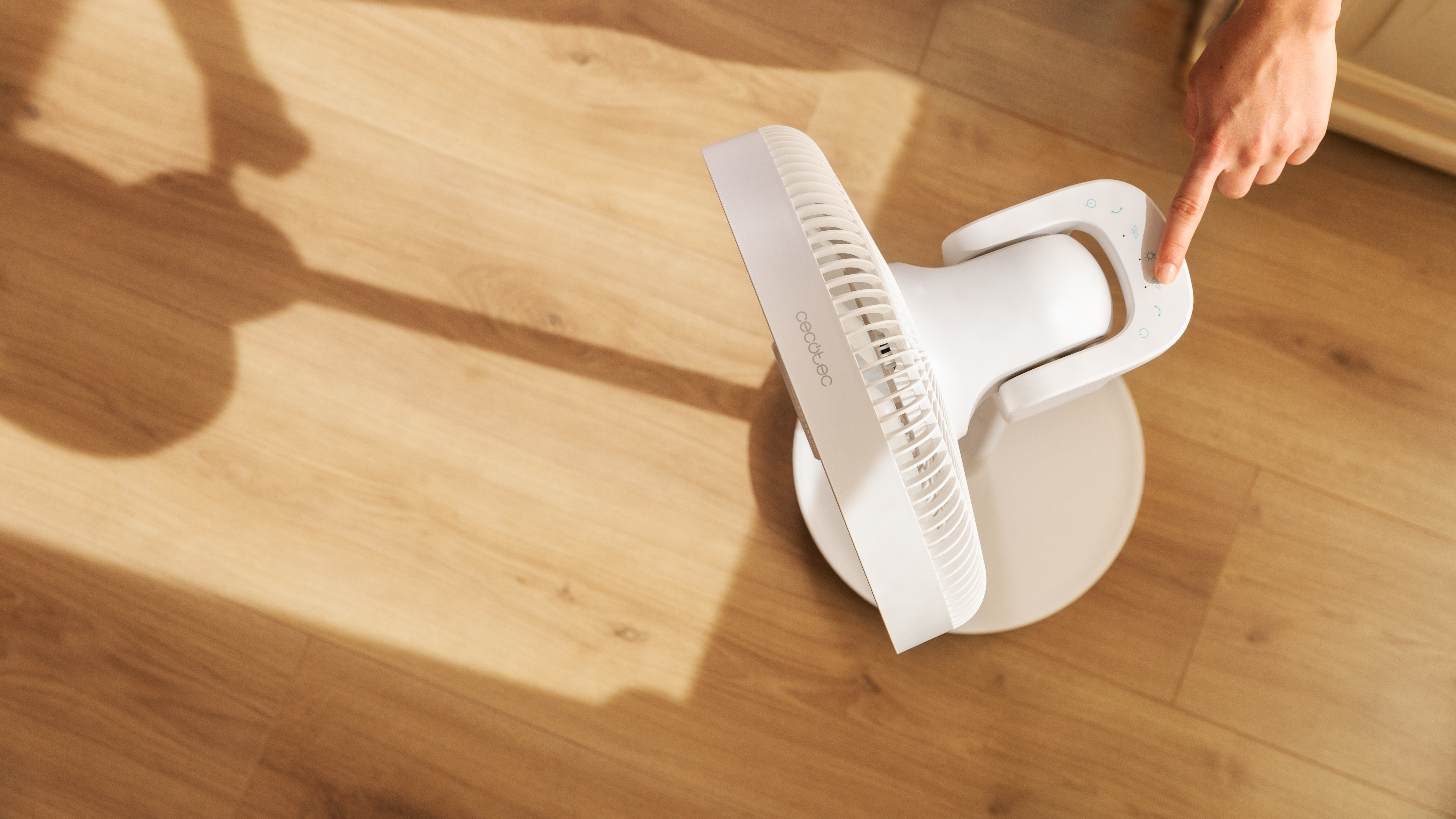 Una persona está presionando un botón en un ventilador blanco con piso de madera.
