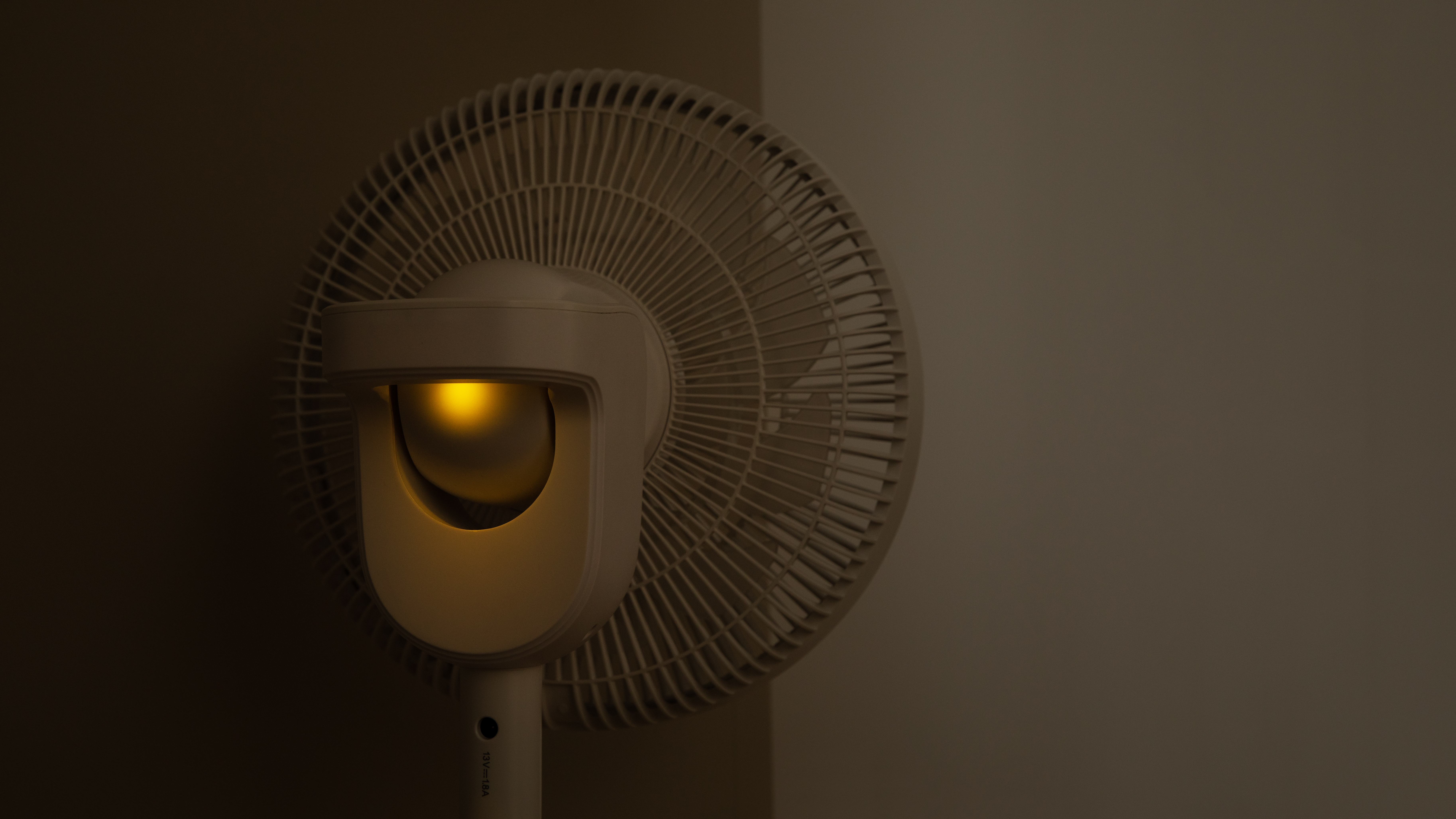 Ventilador blanco con luz amarilla en el interior. Esquina de la habitación. Color claro a la derecha.