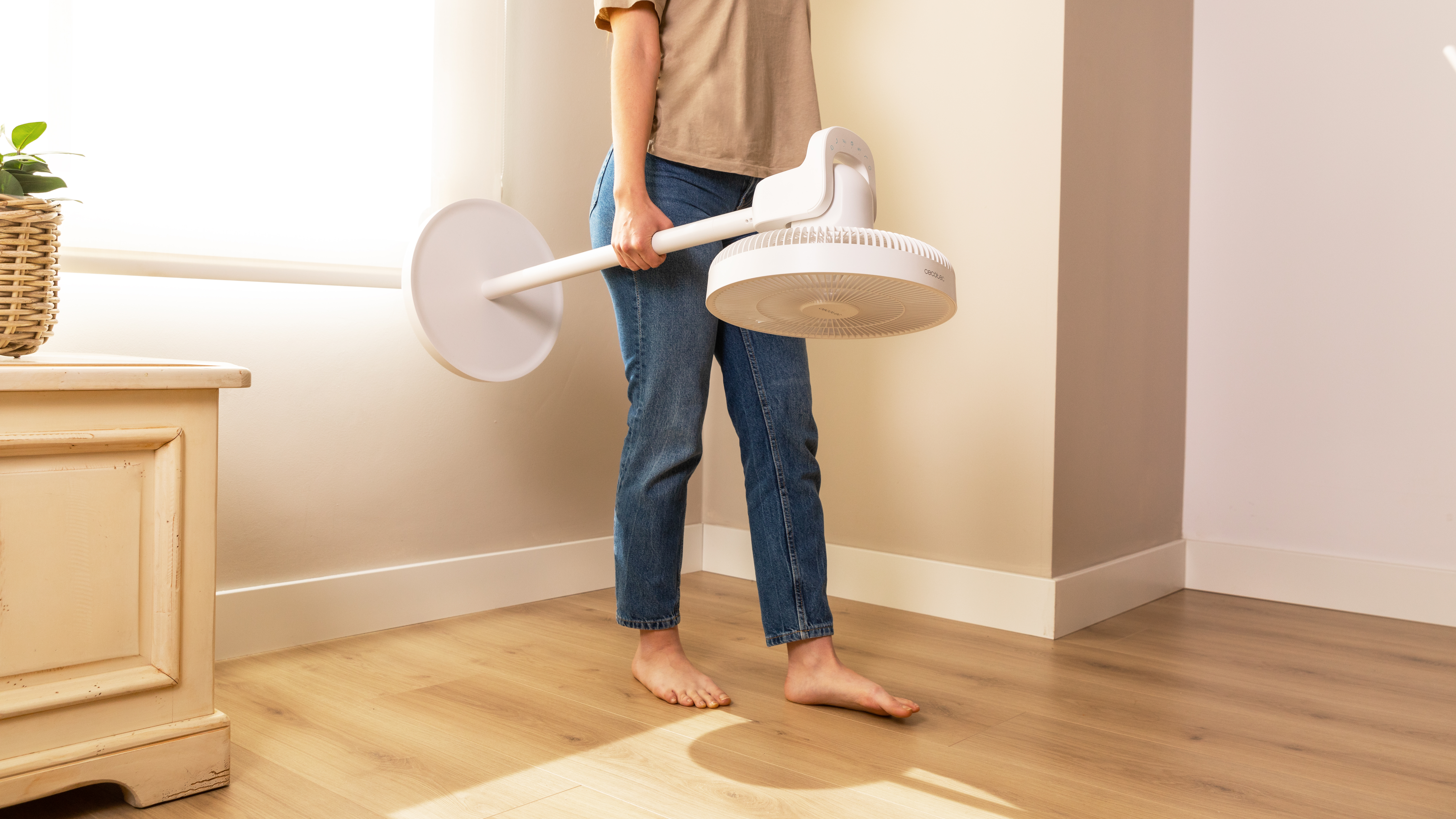 Una persona sosteniendo un ventilador blanco con un poste blanco. El fondo es una habitación.