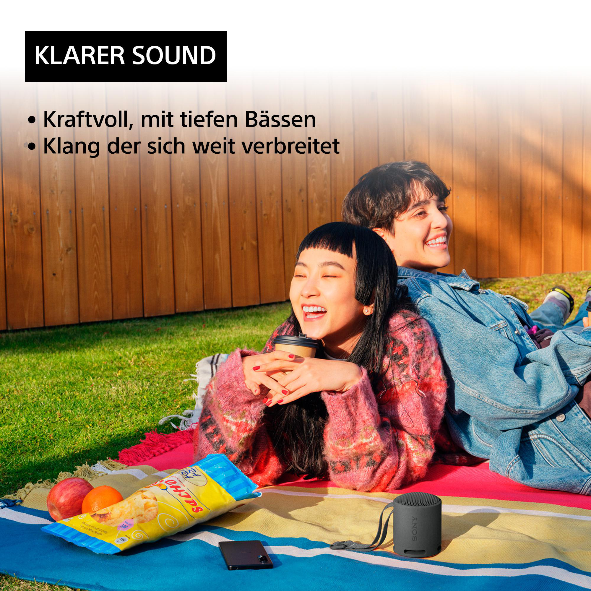 Zwei Personen auf einer Decke mit Lautsprecher, Snacks und Getränken, mit dem Schriftzug "KLARER SOUND".